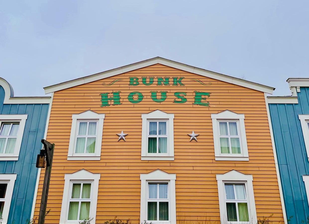 A colorful building with the words "Bunk House" on the facade. The building has multiple windows and a clear sky in the background.