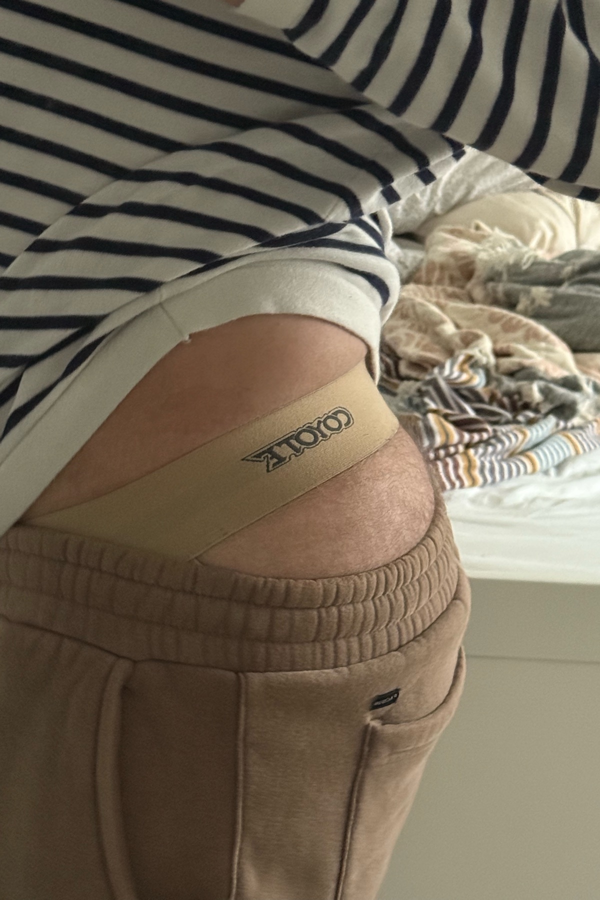 A man is seen from the waist down, wearing a striped shirt and tan sweatpants. His underwear is visible, with a logo on the waistband.