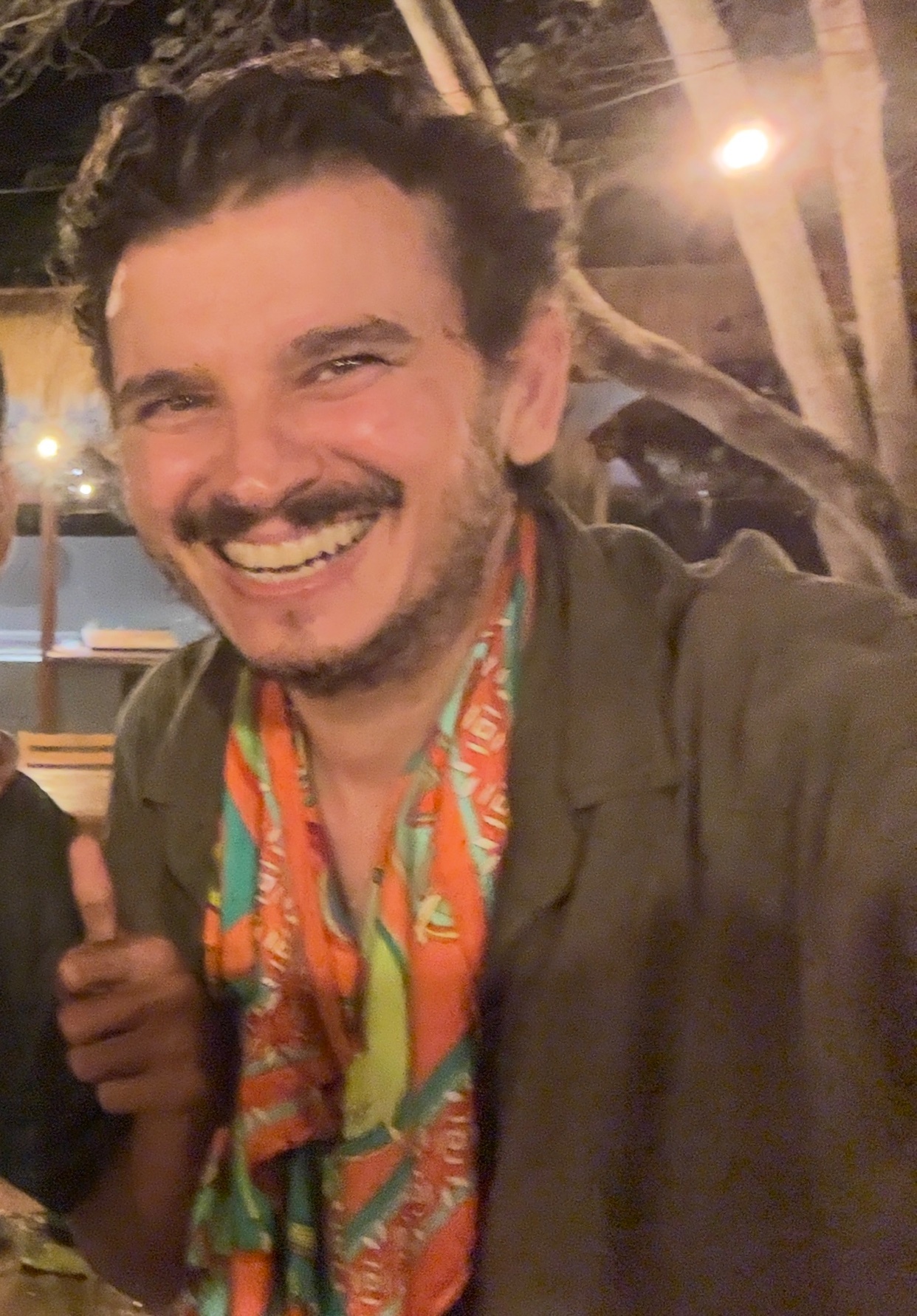 A man smiles at the camera, wearing a scarf and a shirt. The photo is a selfie.