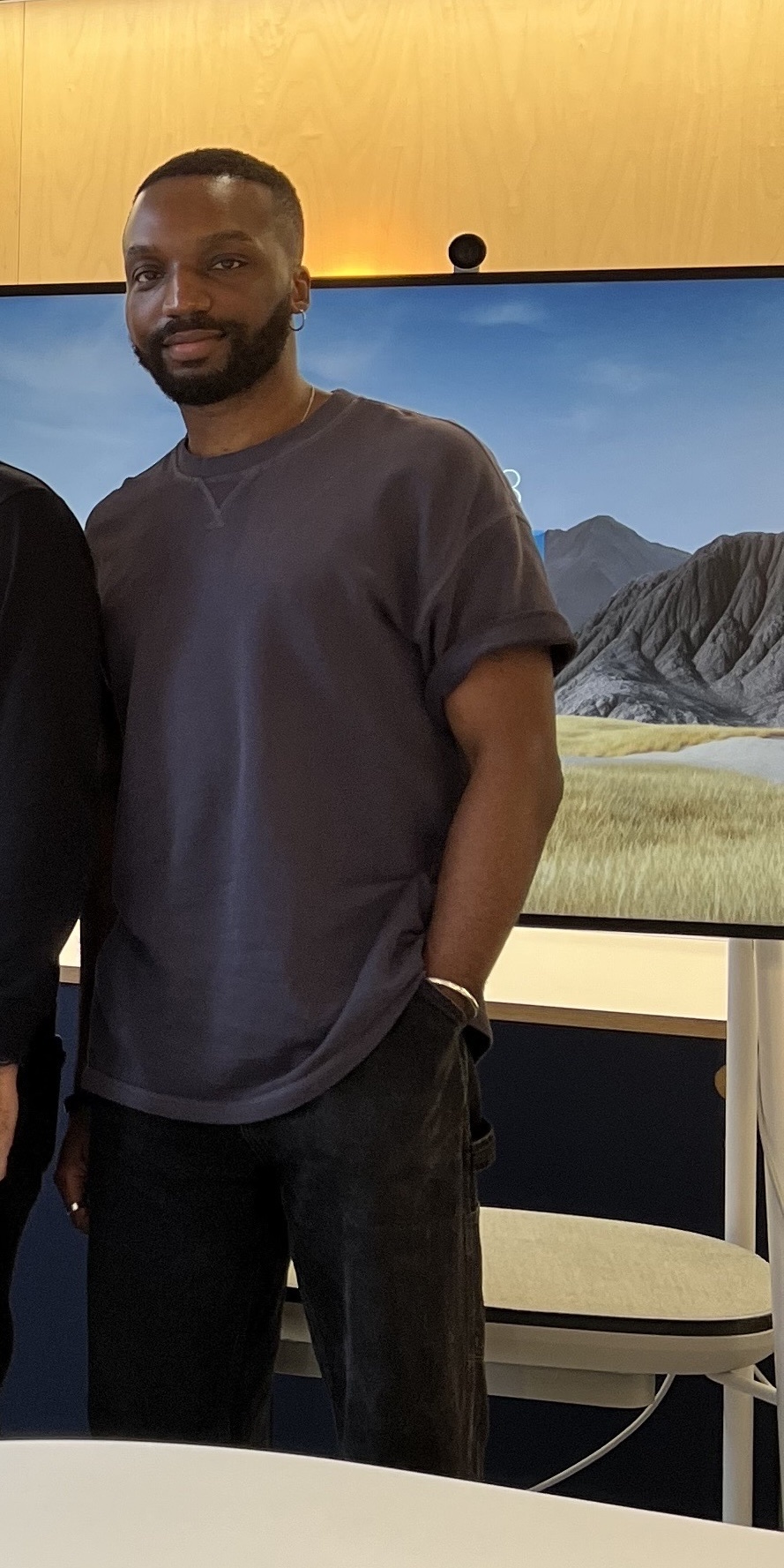 A man poses for a photo. He is wearing a t-shirt and black pants.