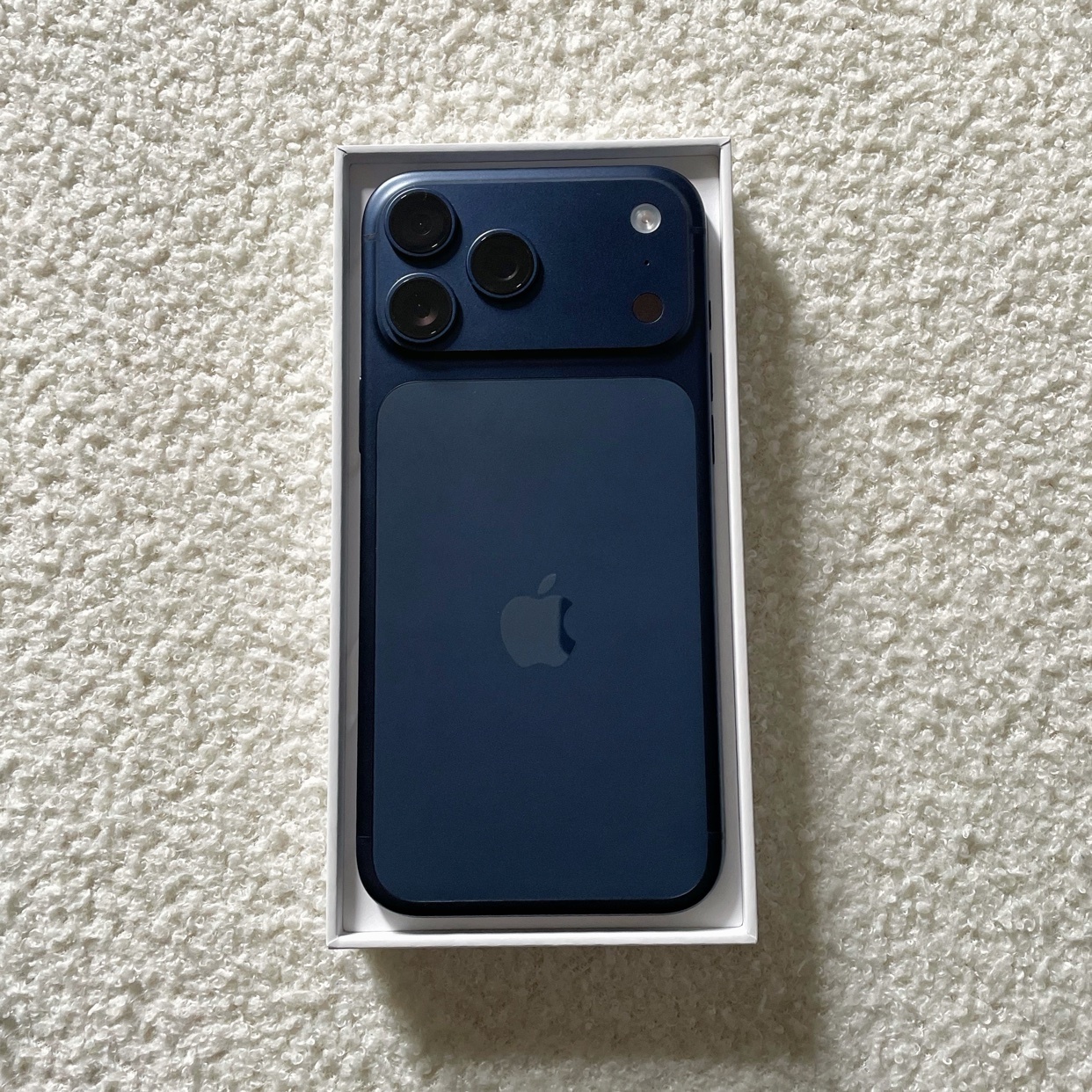 A new blue iPhone sits in its white box. The phone's camera lenses and Apple logo are visible.
