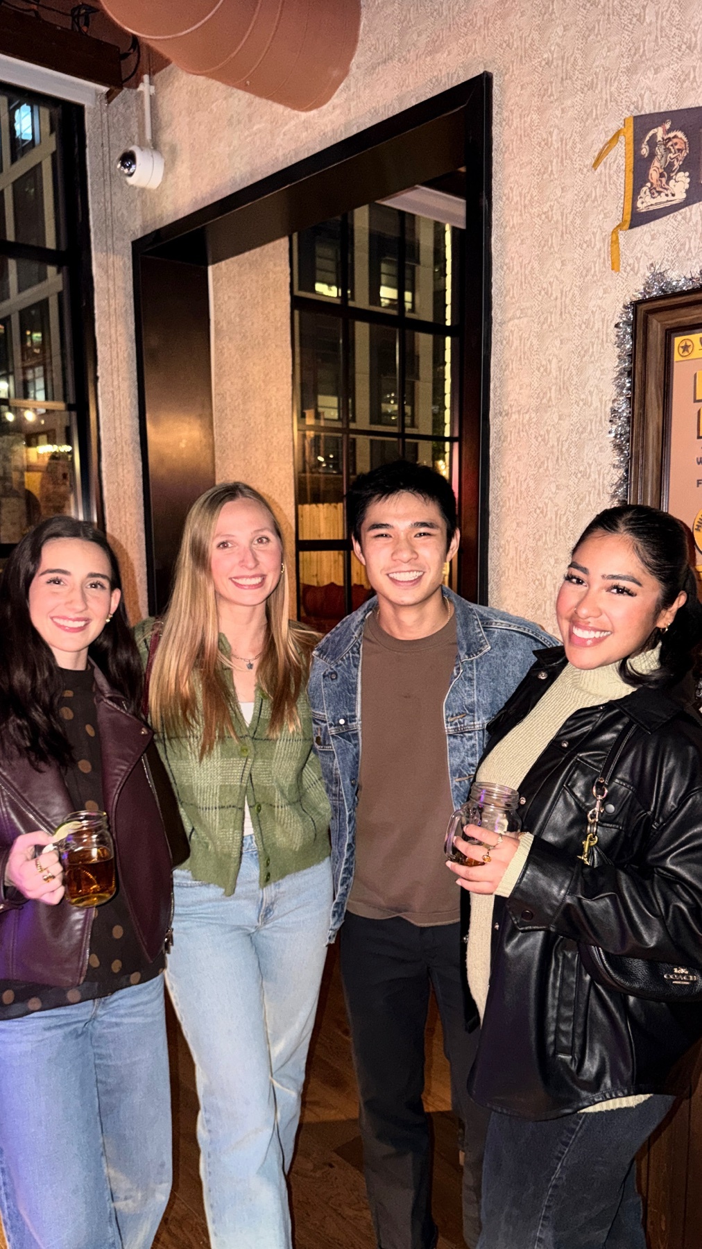 A group of friends pose for a photo inside a pub. They are smiling and holding drinks.