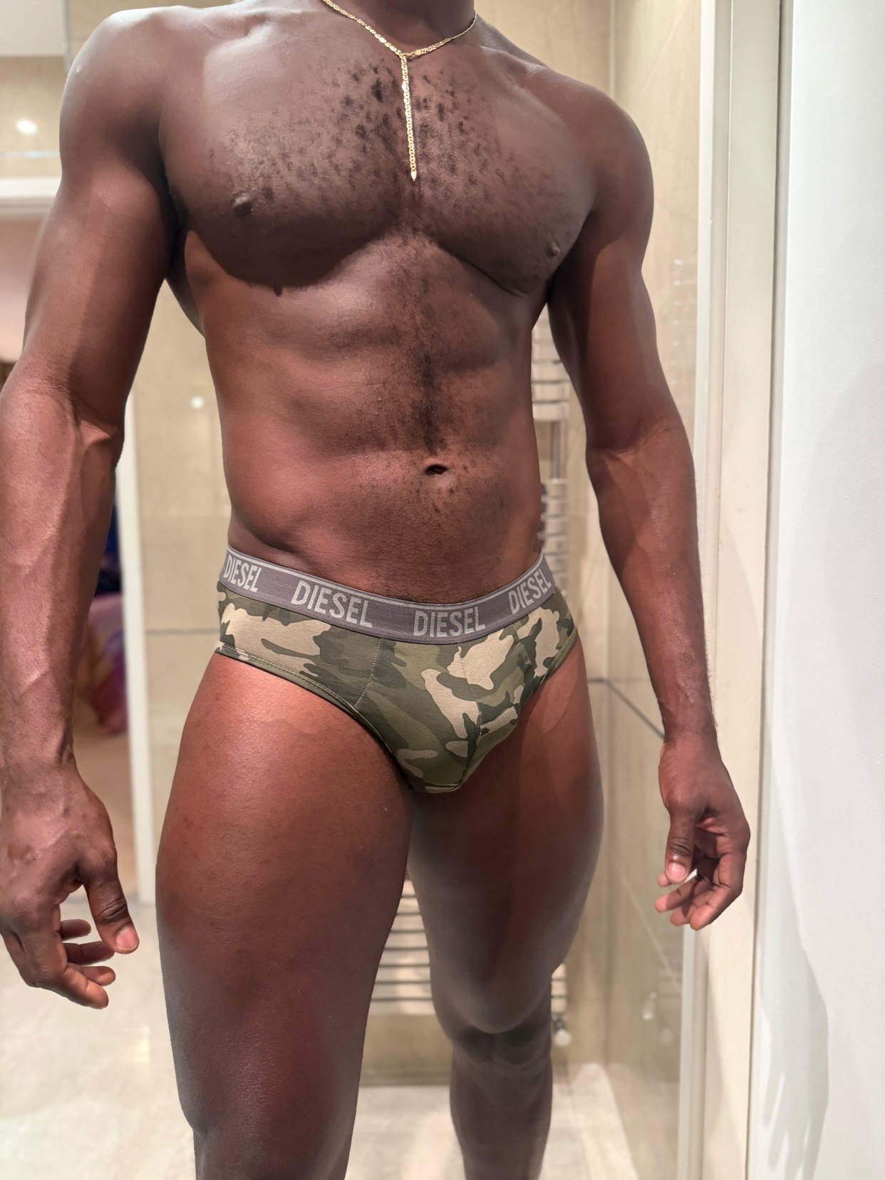 A muscular man poses shirtless in camouflage underwear. The photo highlights his physique and the brand of his underwear.