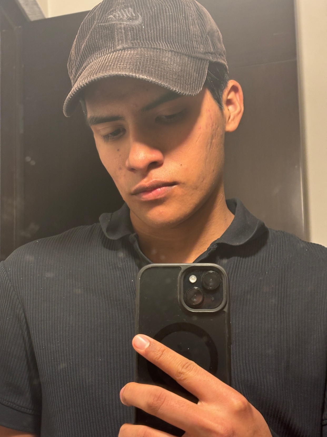 A man takes a selfie in a mirror. He is wearing a cap and a dark shirt.