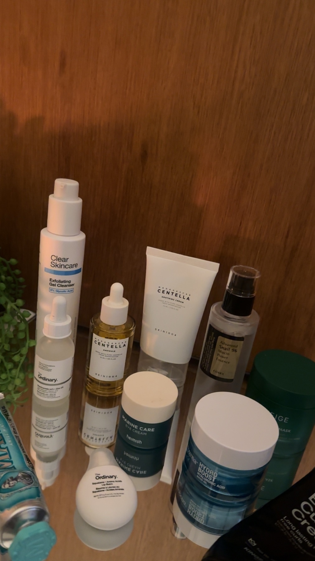 A collection of skincare products is arranged on a reflective surface. The products include various bottles, tubes, and jars, suggesting a skincare routine.