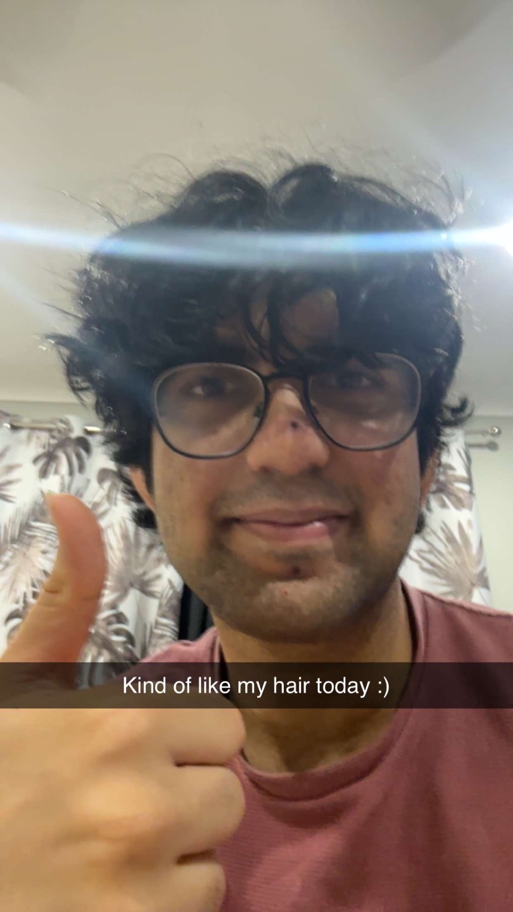A man with curly hair and glasses gives a thumbs up in a selfie. The man is smiling.