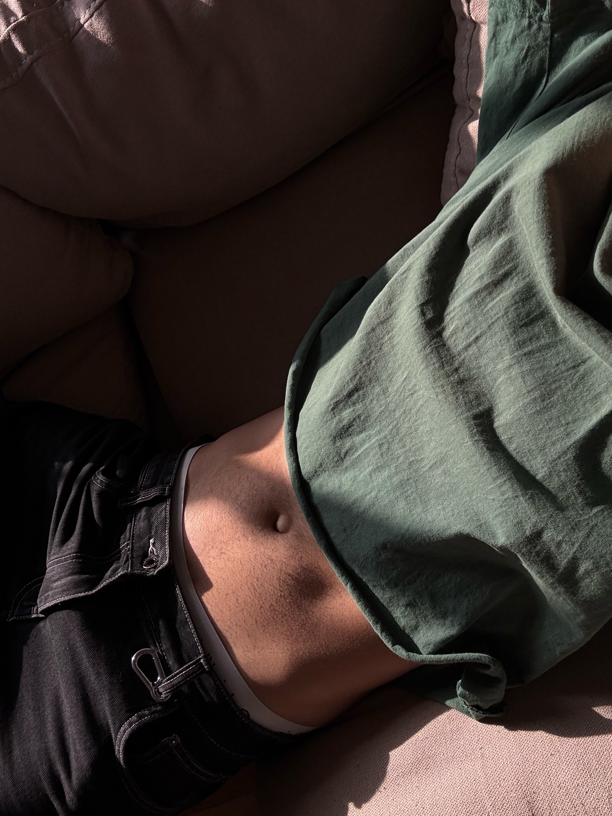 A man is lying on a couch, shirtless, with his stomach visible. The photo is taken in natural light, creating shadows and highlights.
