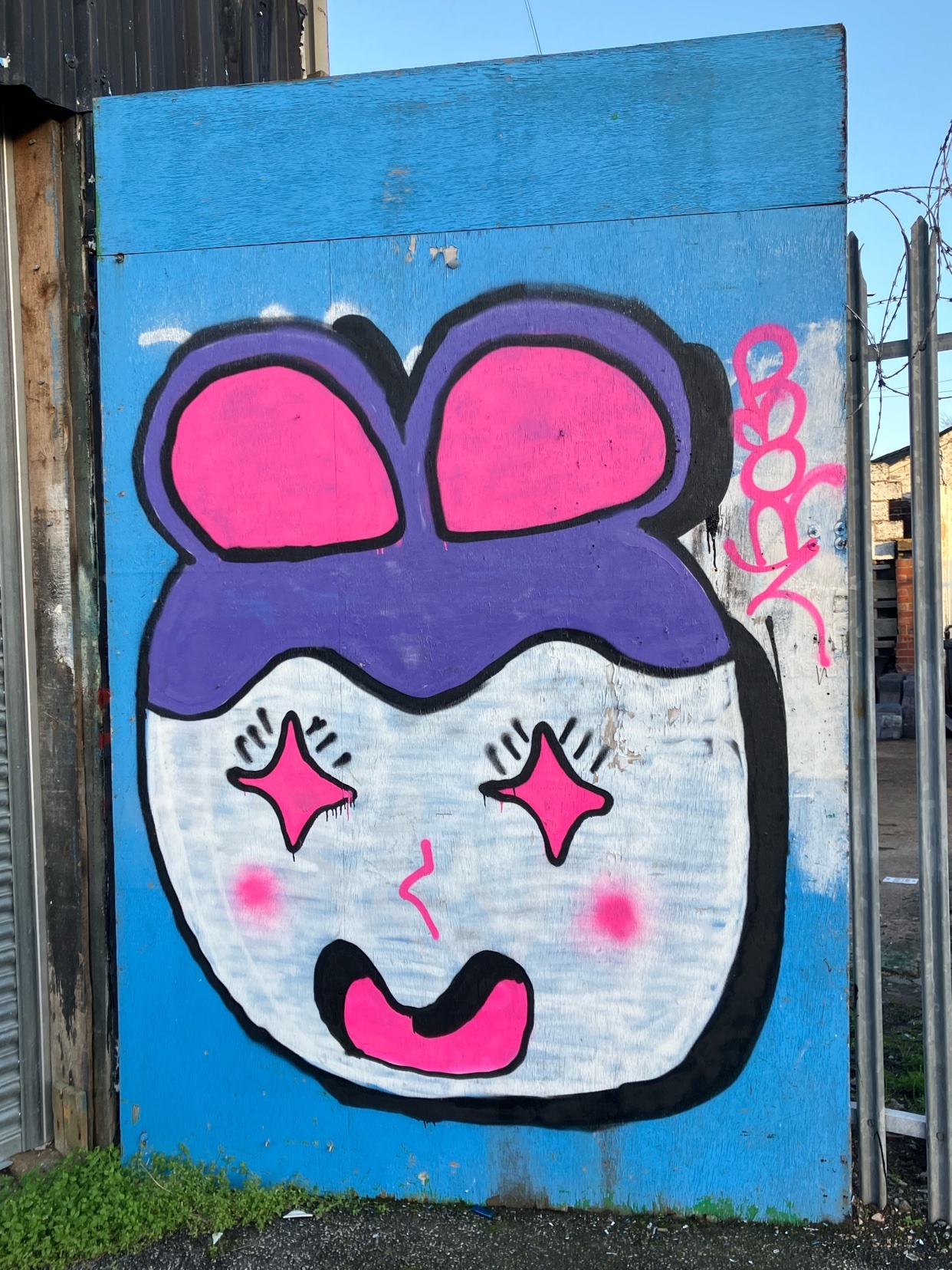 A colorful graffiti art piece on a blue background. The artwork features a cartoon face with pink accents and star-shaped eyes.