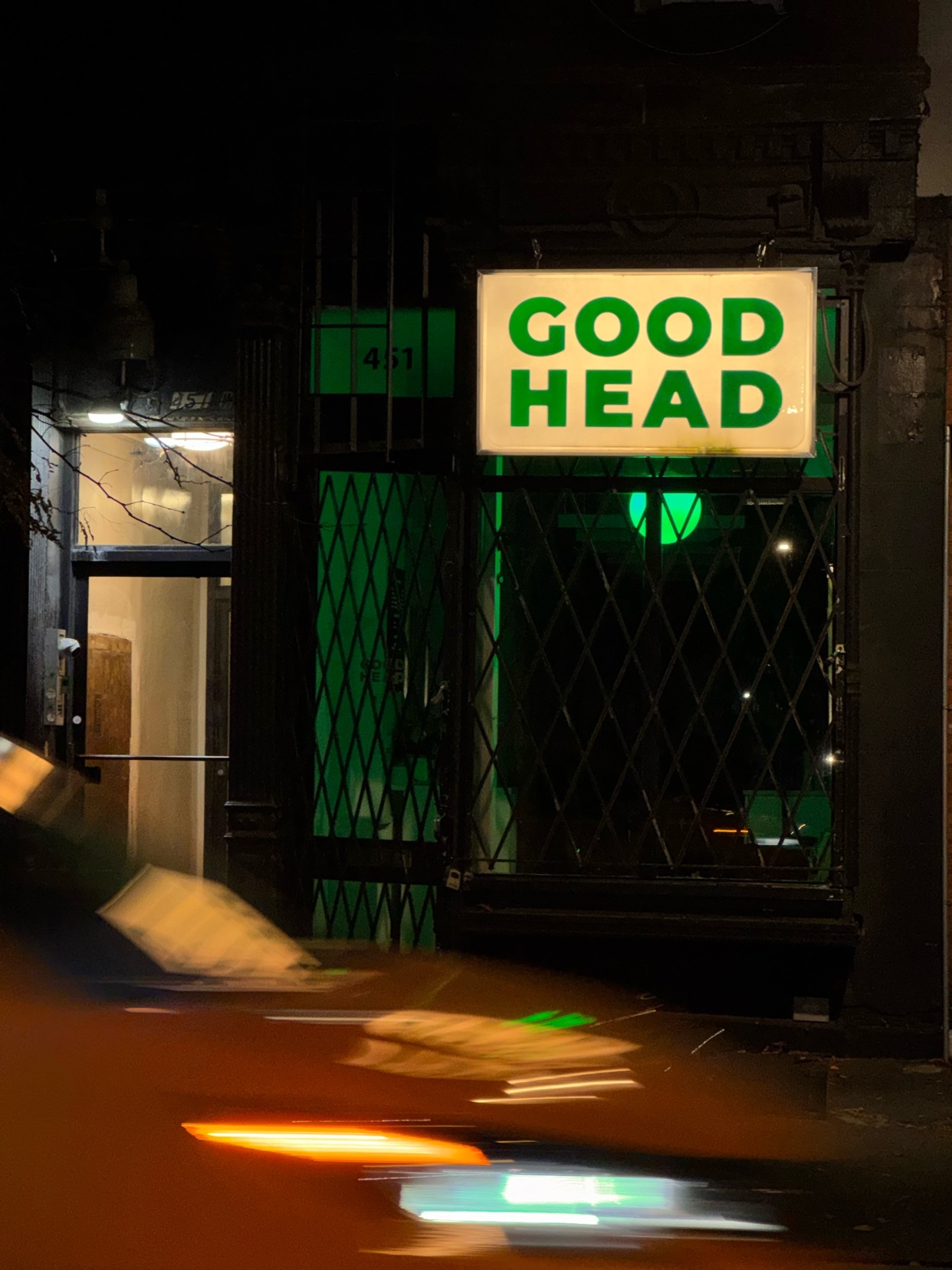 A neon sign that says "Good Head" is lit up at night. The image is taken from a street view.