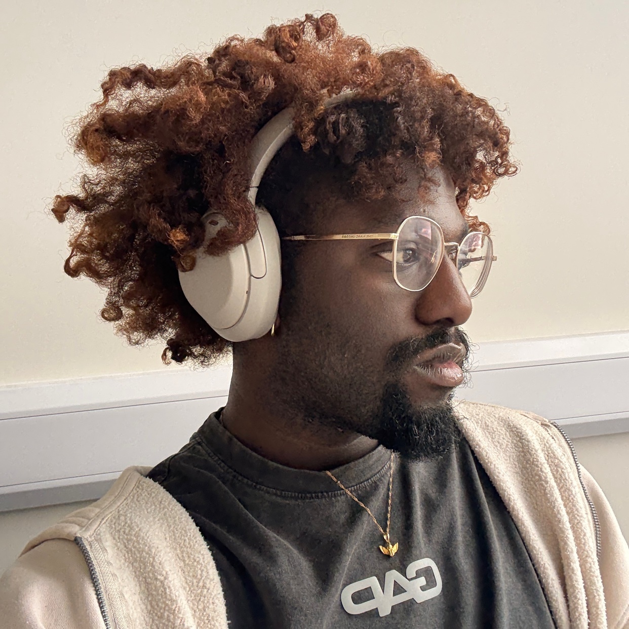 A man with curly brown hair and glasses wears headphones and a t-shirt. He is looking off to the side.