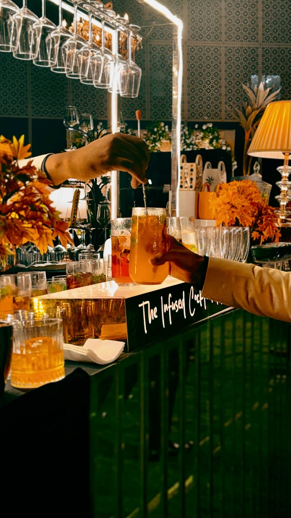 A bartender pours a cocktail at a bar. The photo showcases the preparation of a drink with various glasses and bottles in the background.