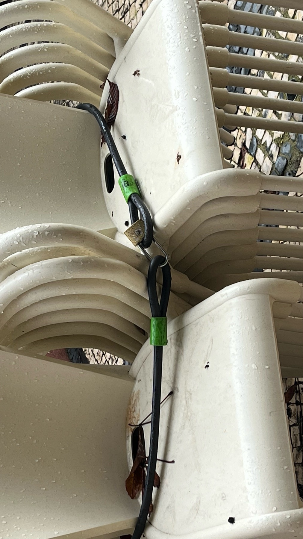 A stack of white plastic chairs, secured with a black cable. The chairs are arranged in a neat pile, suggesting outdoor use.