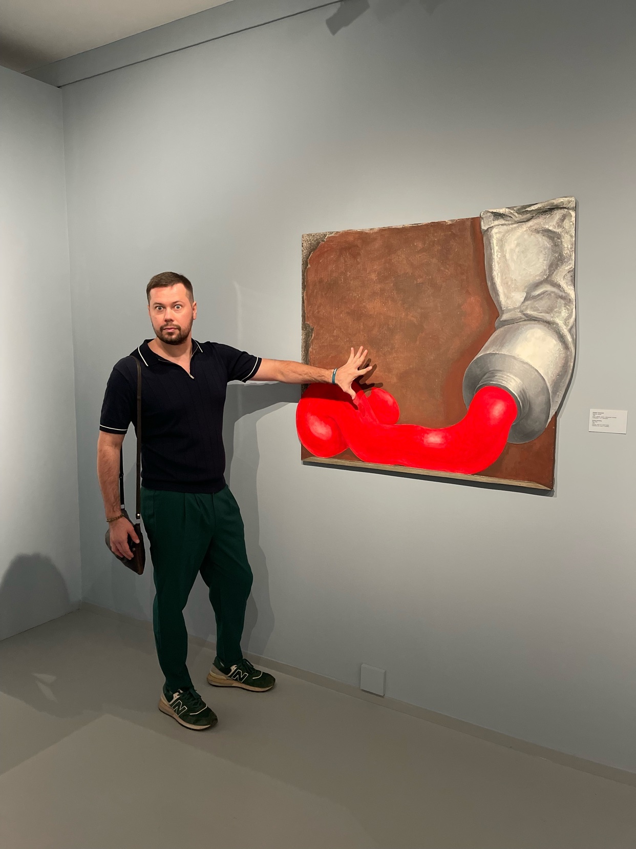A man poses next to a 3D painting of a tube of paint. The artwork is a vibrant display of color and form.