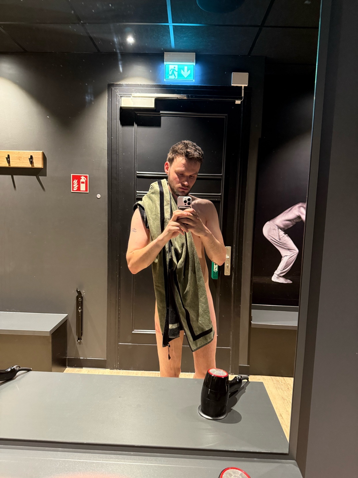 A man takes a mirror selfie in a locker room, holding a towel.