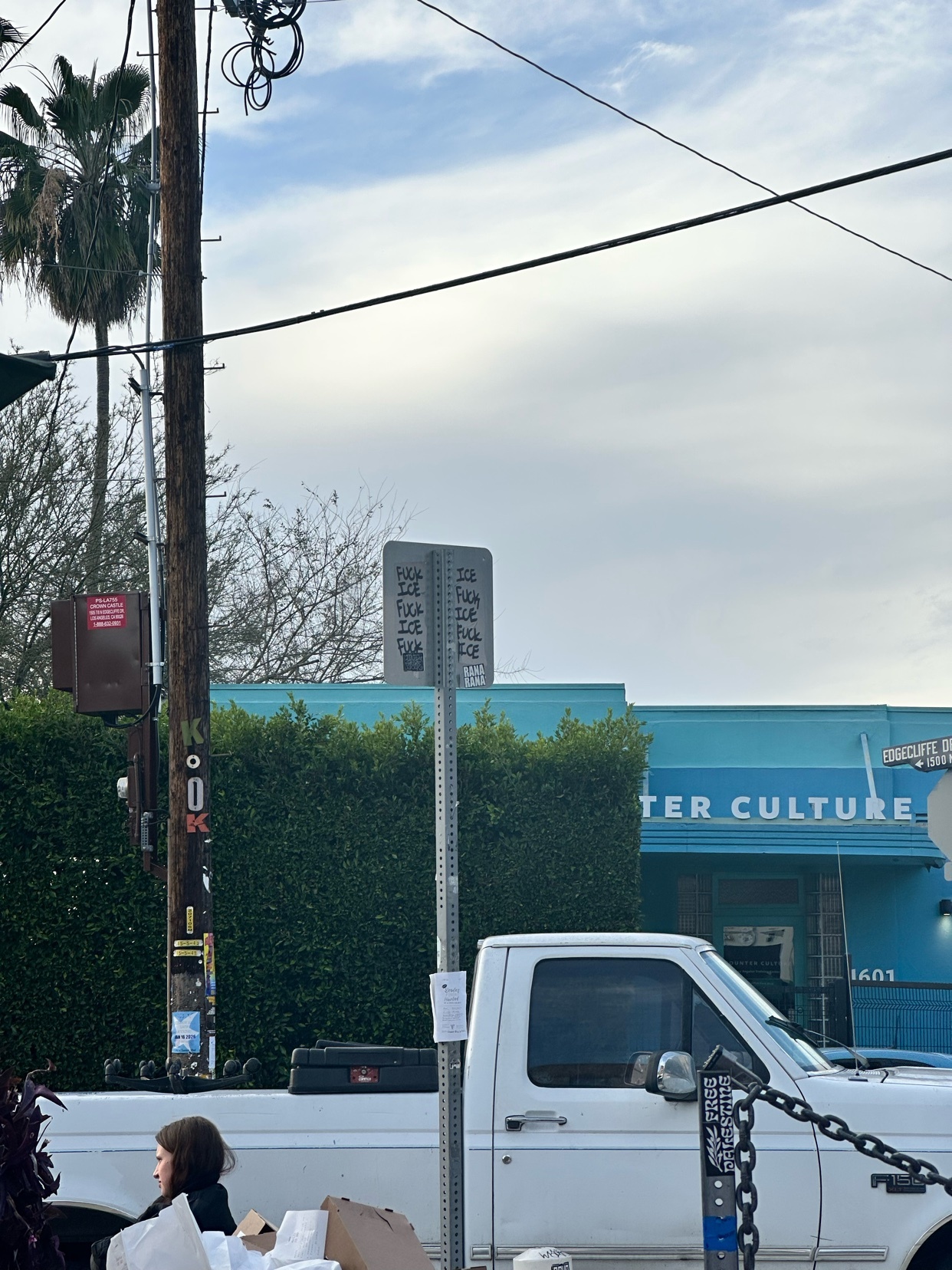 A street scene with a truck, a sign, and a building. The sky is cloudy.