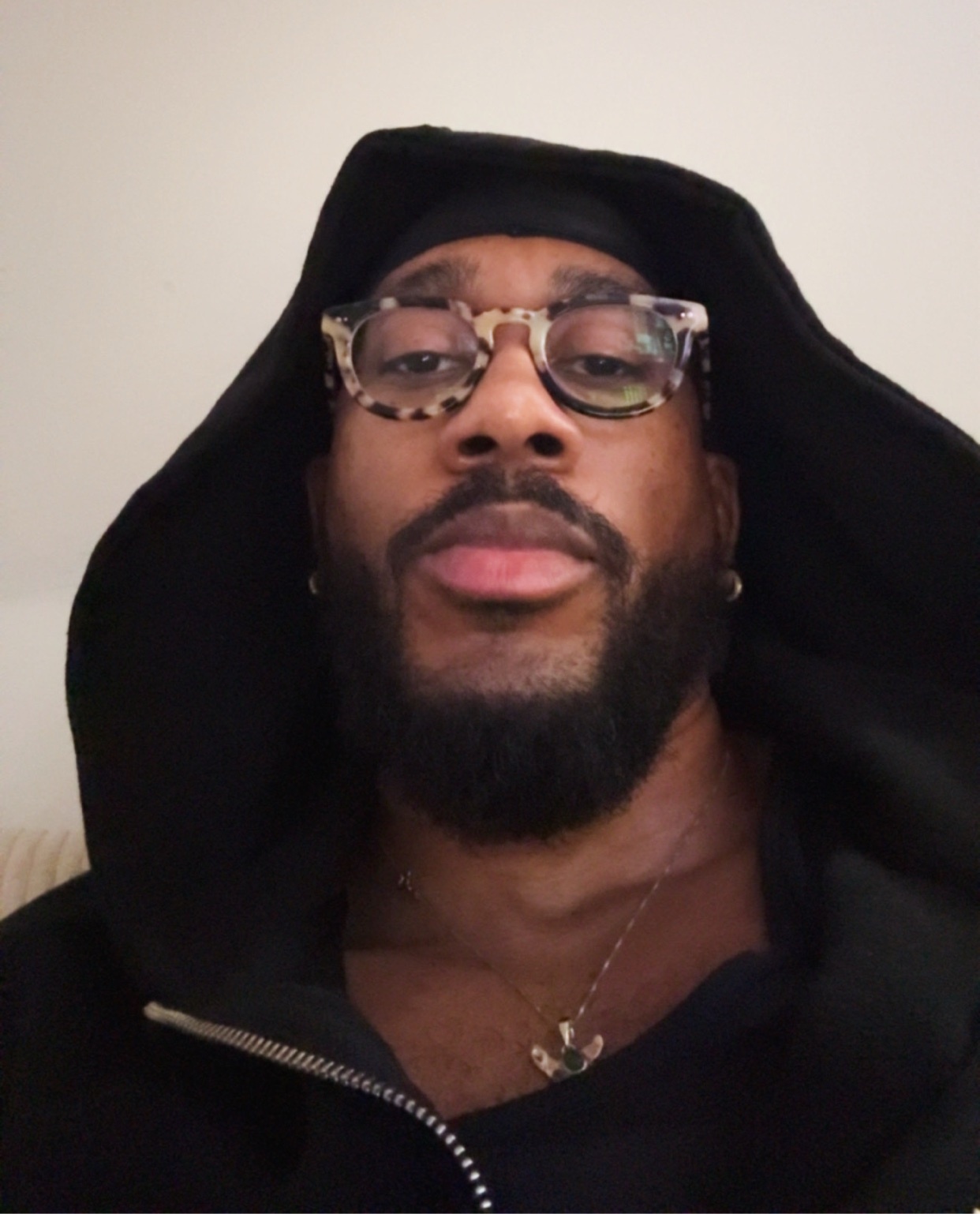A man with a beard and glasses poses for a selfie. He is wearing a black hoodie.