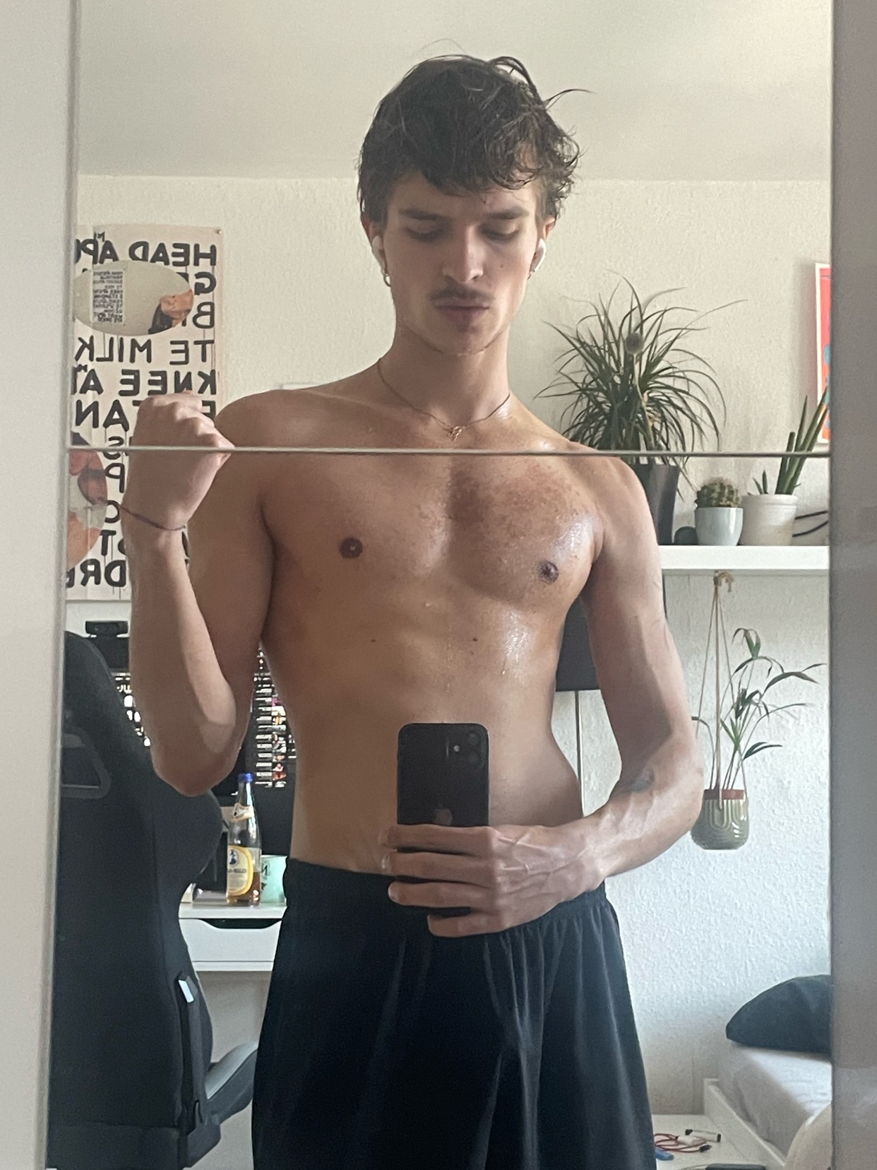 A man poses shirtless in front of a mirror, showcasing his physique. The photo is a mirror selfie, highlighting his muscular build and physique.