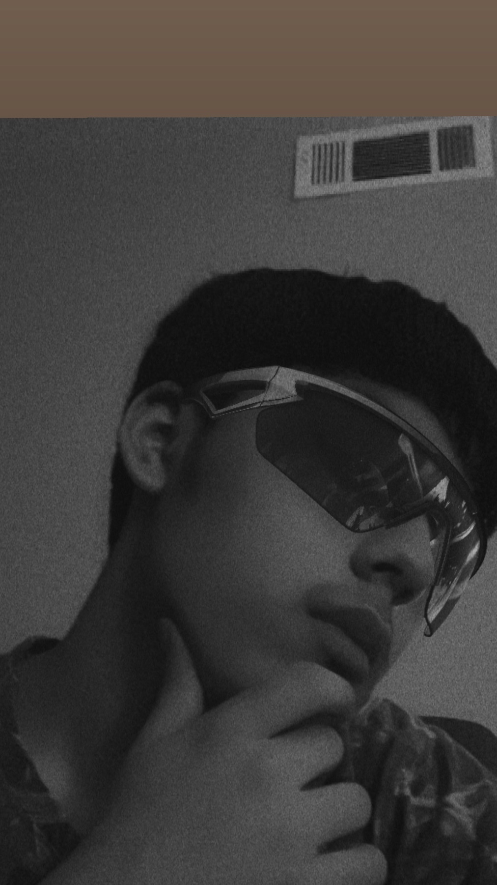 A black and white close-up selfie of a young man wearing sunglasses and resting his chin on his hand.