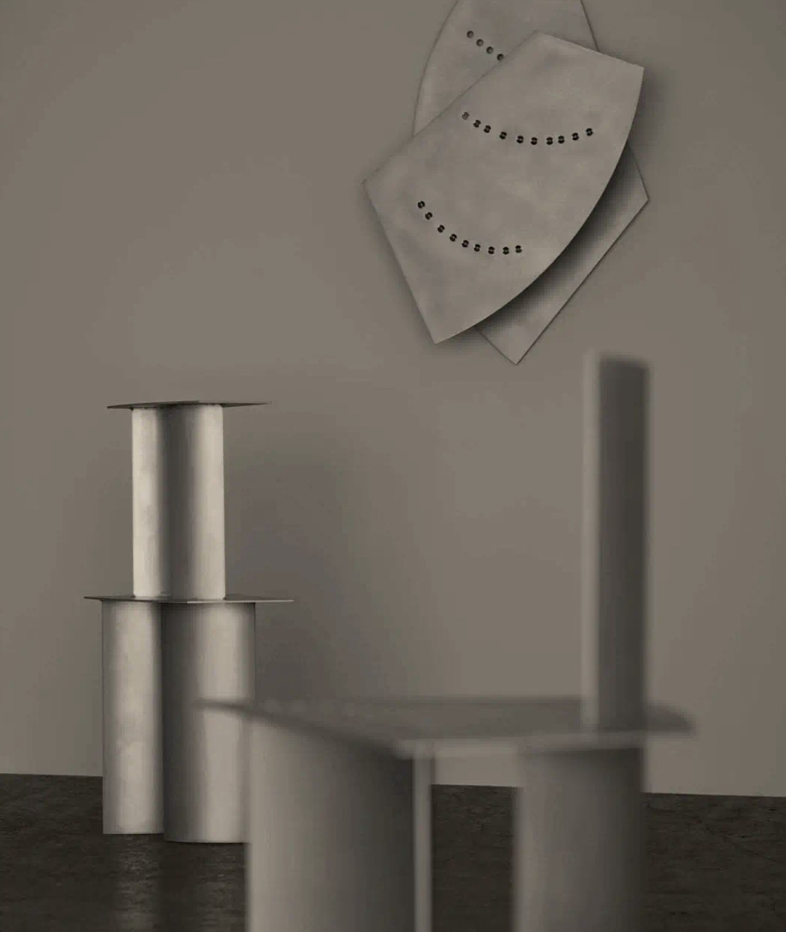 An abstract sculpture with geometric shapes and a minimalist design. The artwork is made of metal and is displayed on a gray wall.
