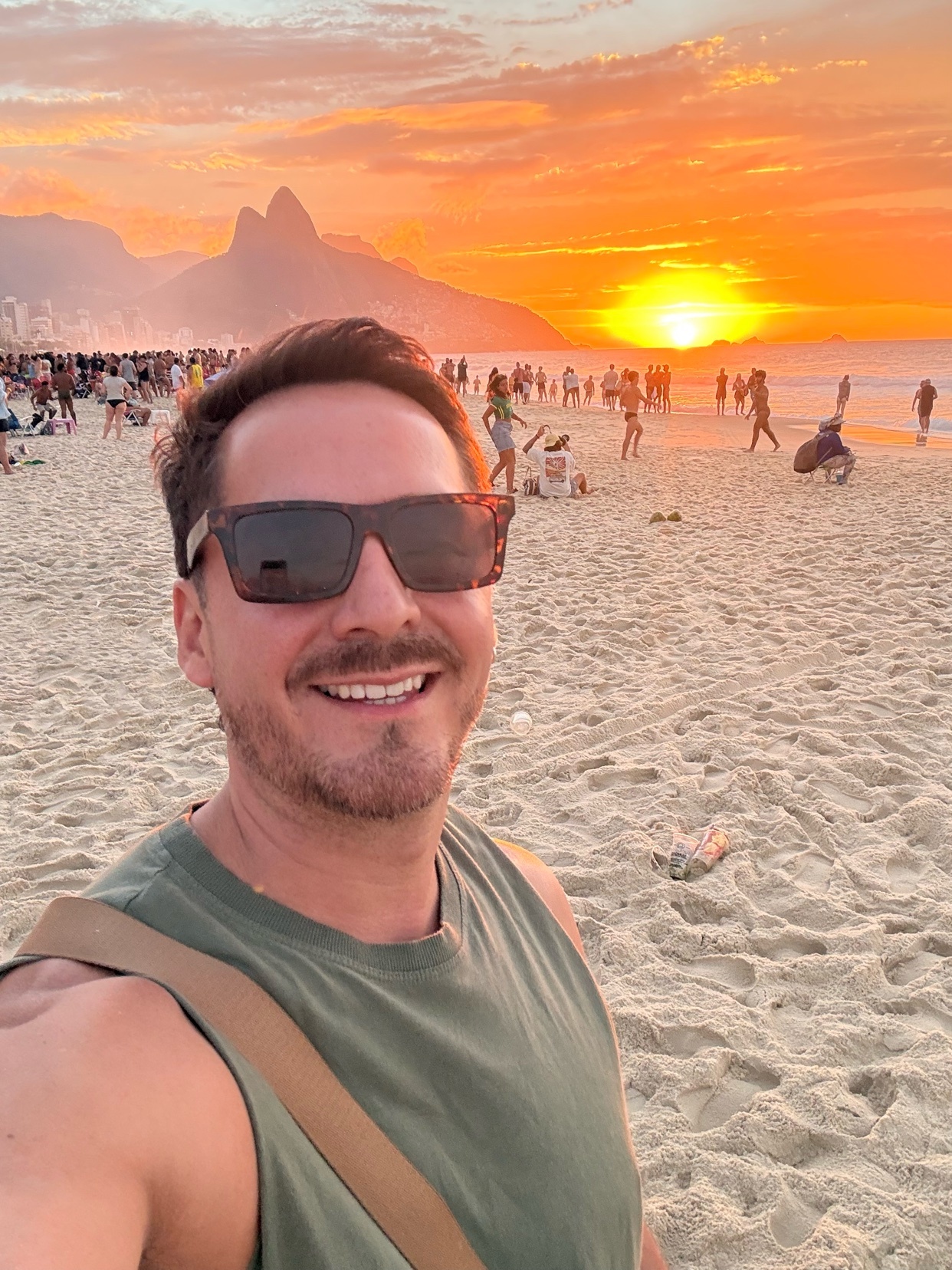 A man takes a selfie on a beach at sunset. The photo captures the vibrant colors of the sky and the beach scene.