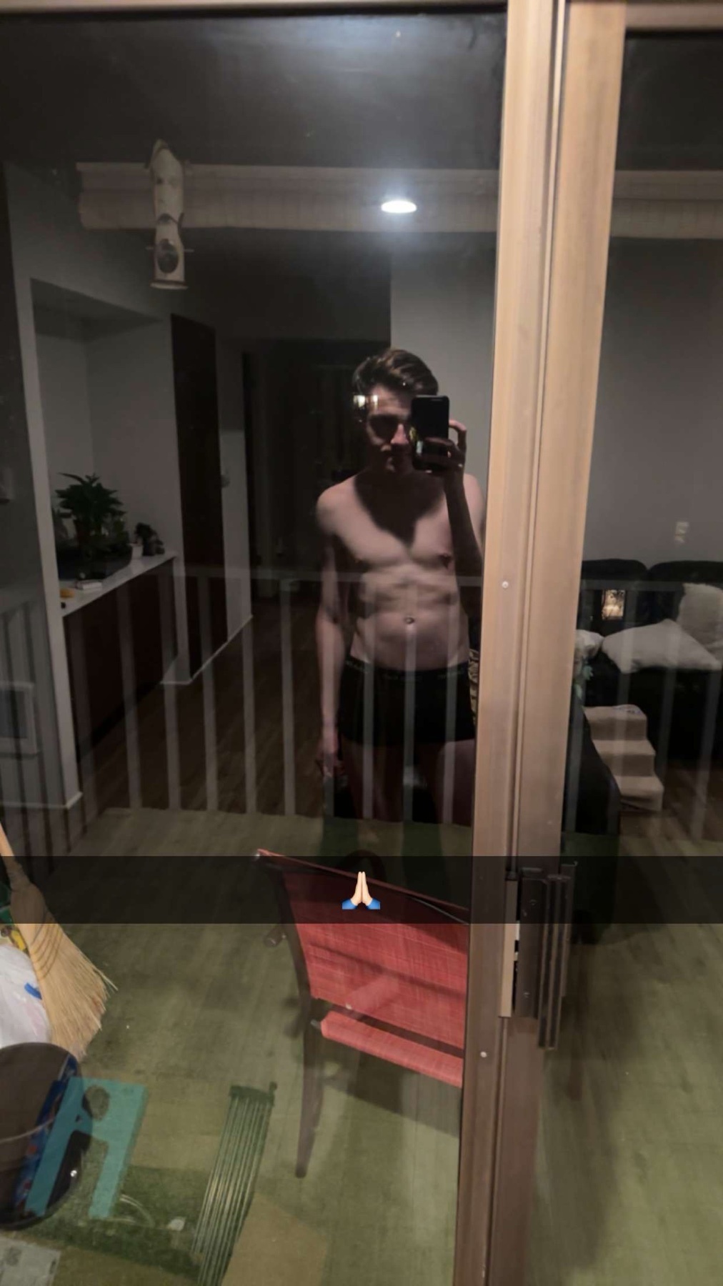 A man takes a shirtless mirror selfie, showcasing his physique. The reflection captures the interior of a home.