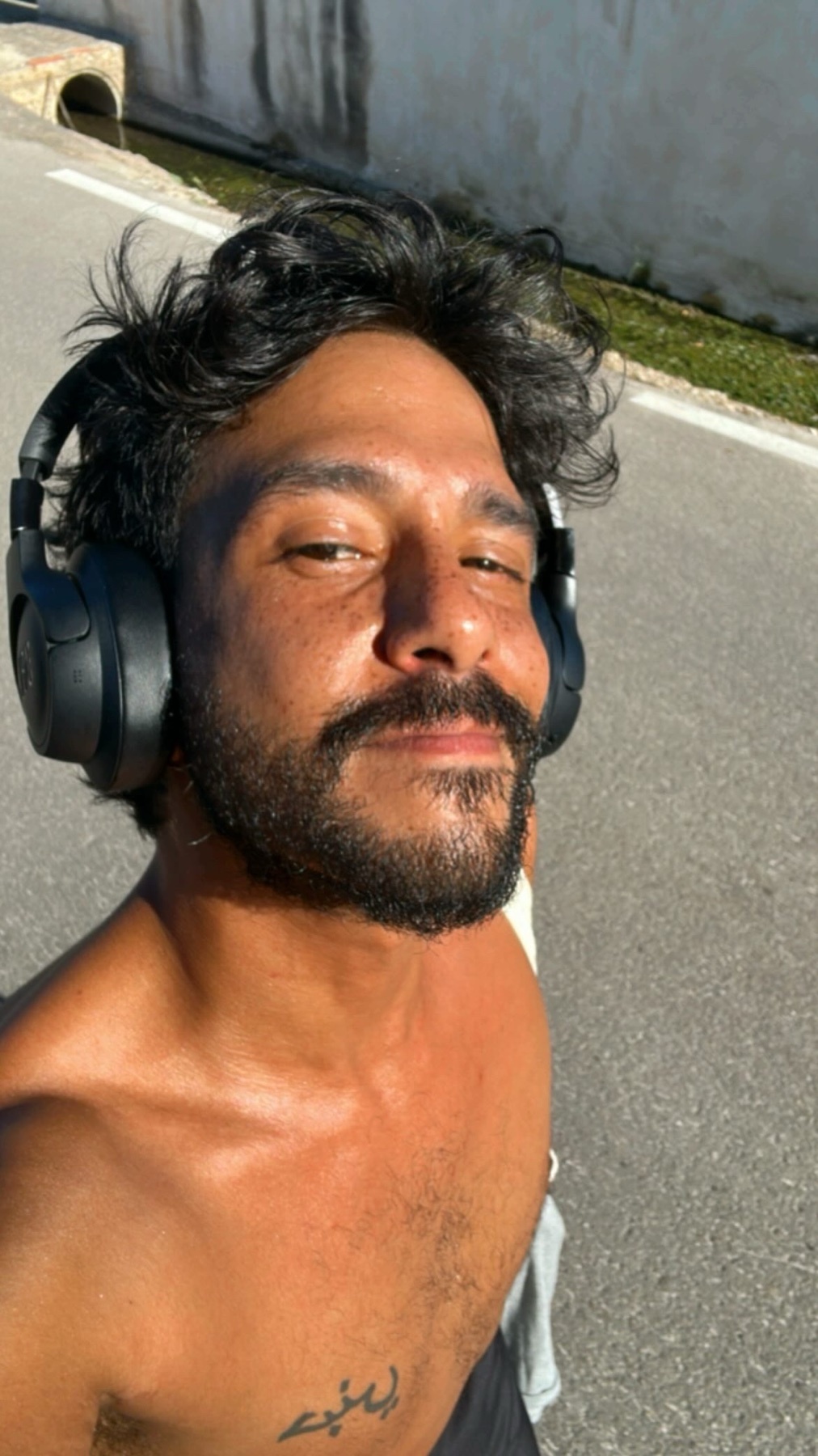 A man is running shirtless while wearing headphones. The photo is taken outdoors on a sunny day.