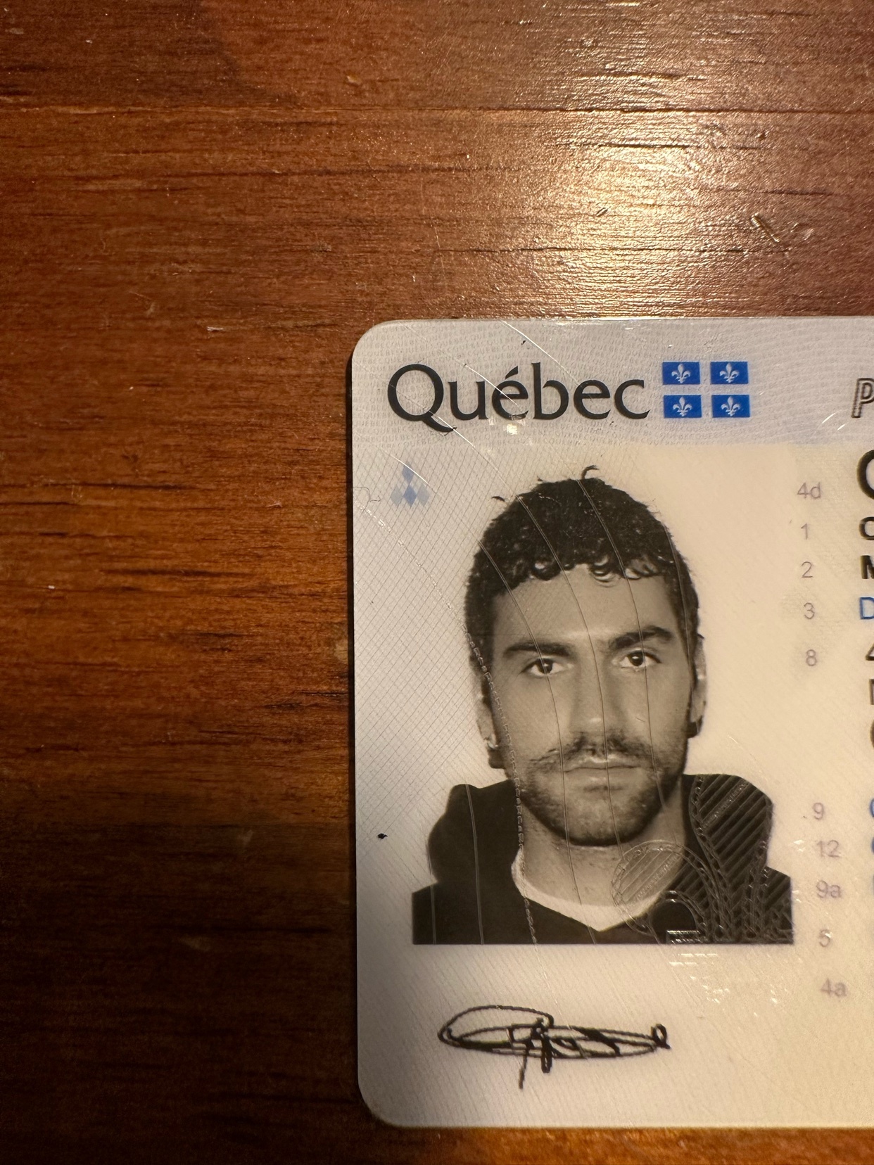 A close-up photo of a Quebec identity card featuring a man's portrait. The card is placed on a wooden surface.