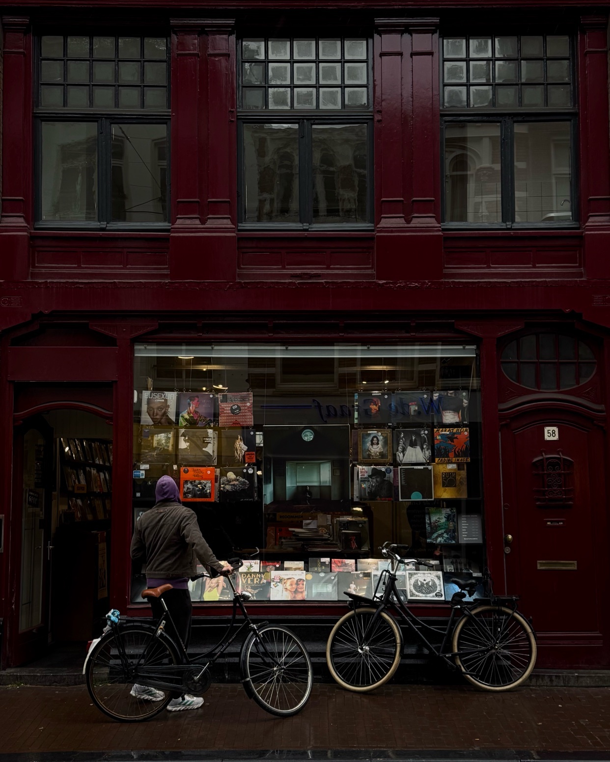 A man stands outside a record store, admiring the vinyl records on display. Two bicycles are parked in front of the shop.