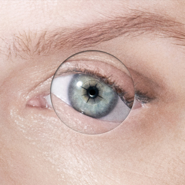 A close-up shot of a human eye with a blue iris. A lens is placed over the eye, creating an optical illusion.