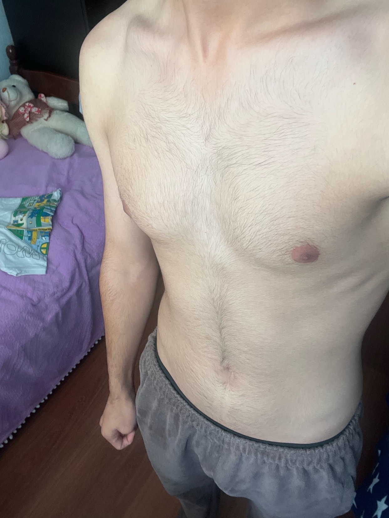 A shirtless man poses for a photo, showcasing his physique. The image highlights his chest hair and muscular build.