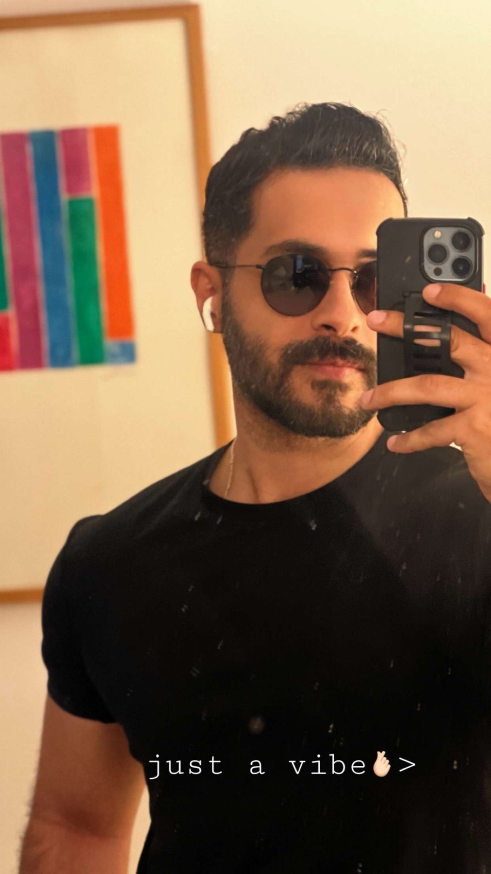 A man takes a selfie in a black t-shirt and sunglasses, with earbuds in his ears. He has stubble and a moustache, and the text 'just a vibe' is overlaid on the image.