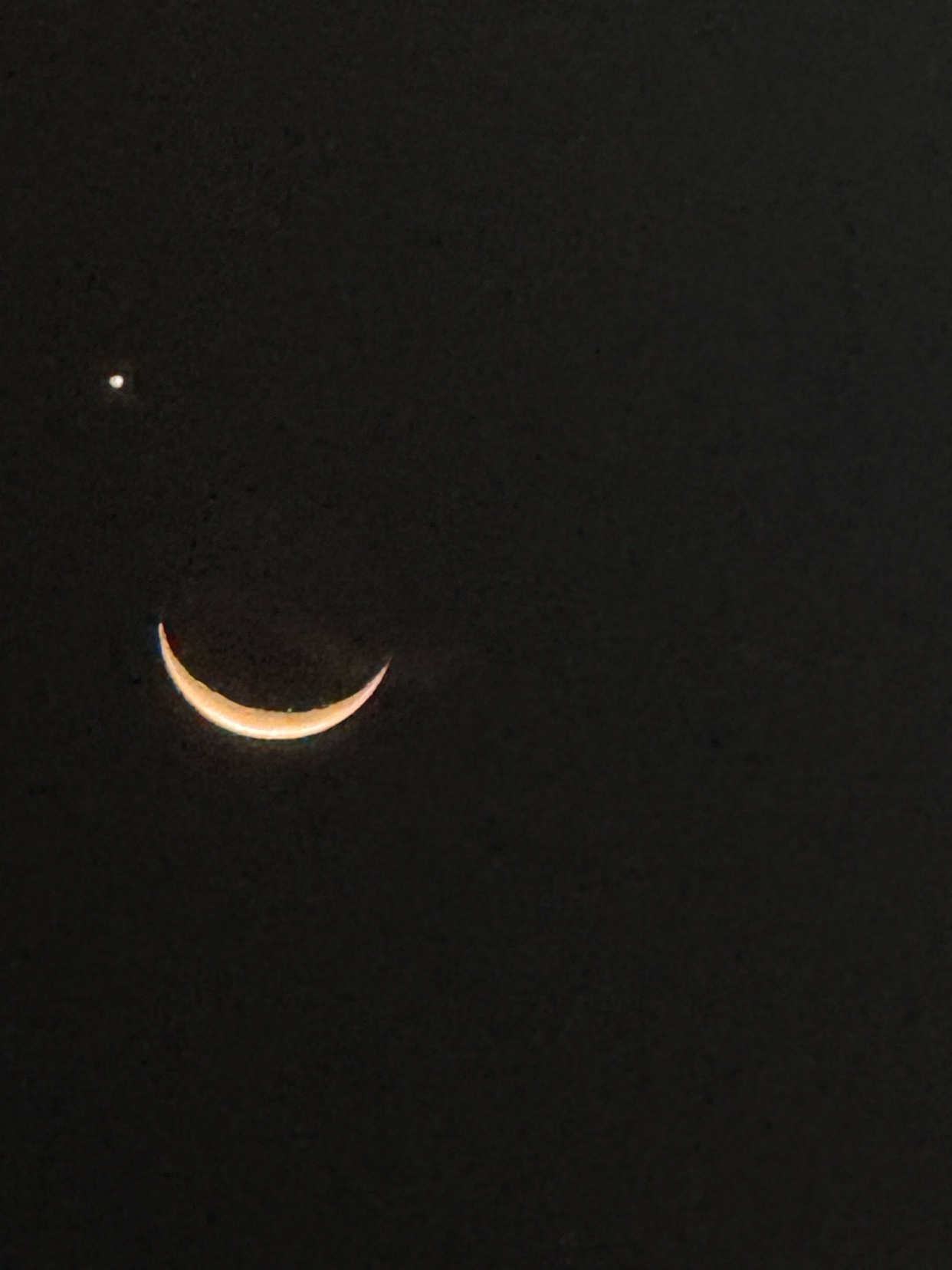 A thin crescent moon hangs in the dark night sky, accompanied by a bright planet nearby.