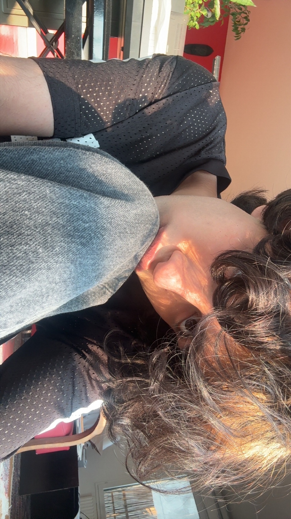 A close-up, low-angle shot of a woman's face bathed in warm sunlight. Her long, curly hair frames her face as she looks down, with the light casting dramatic shadows and highlights.