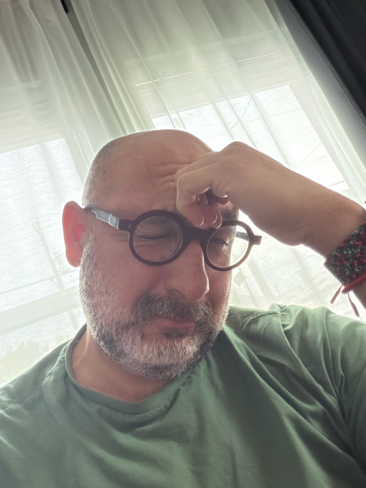 A man with a bald head and glasses is holding his forehead, appearing stressed or tired.