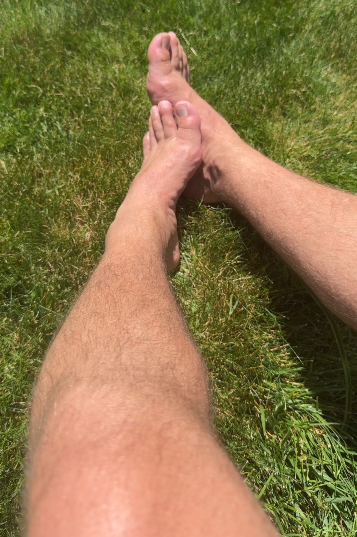 A close-up shot of a person's bare feet and legs resting on lush green grass on a sunny day.