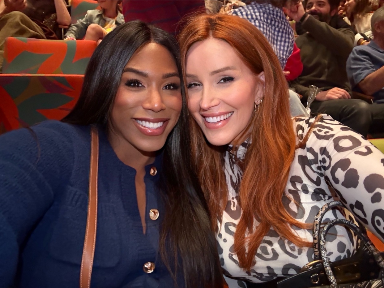 Two women smile for a selfie at a concert hall. They are close together, appearing happy and friendly.