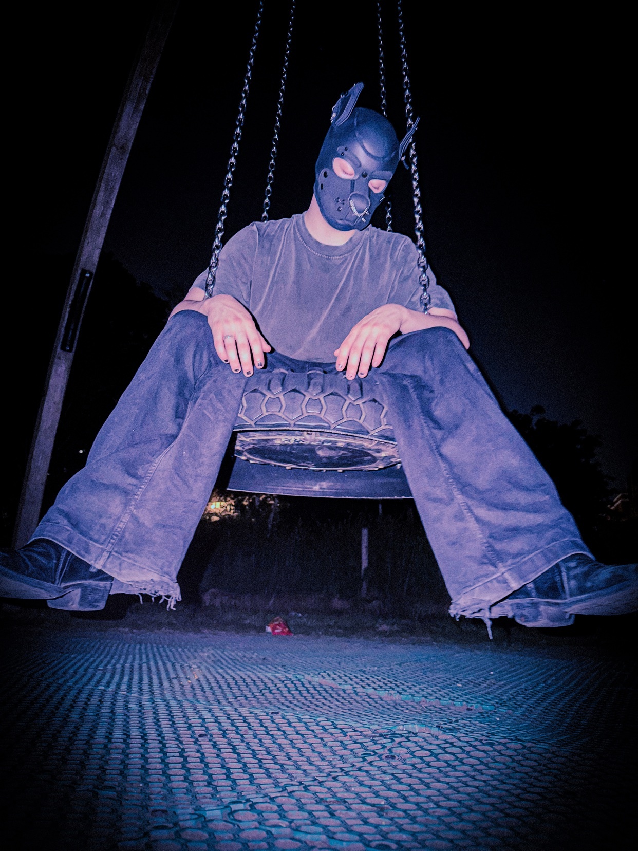 A person wearing a puppy mask and costume sits on a swing set at night.