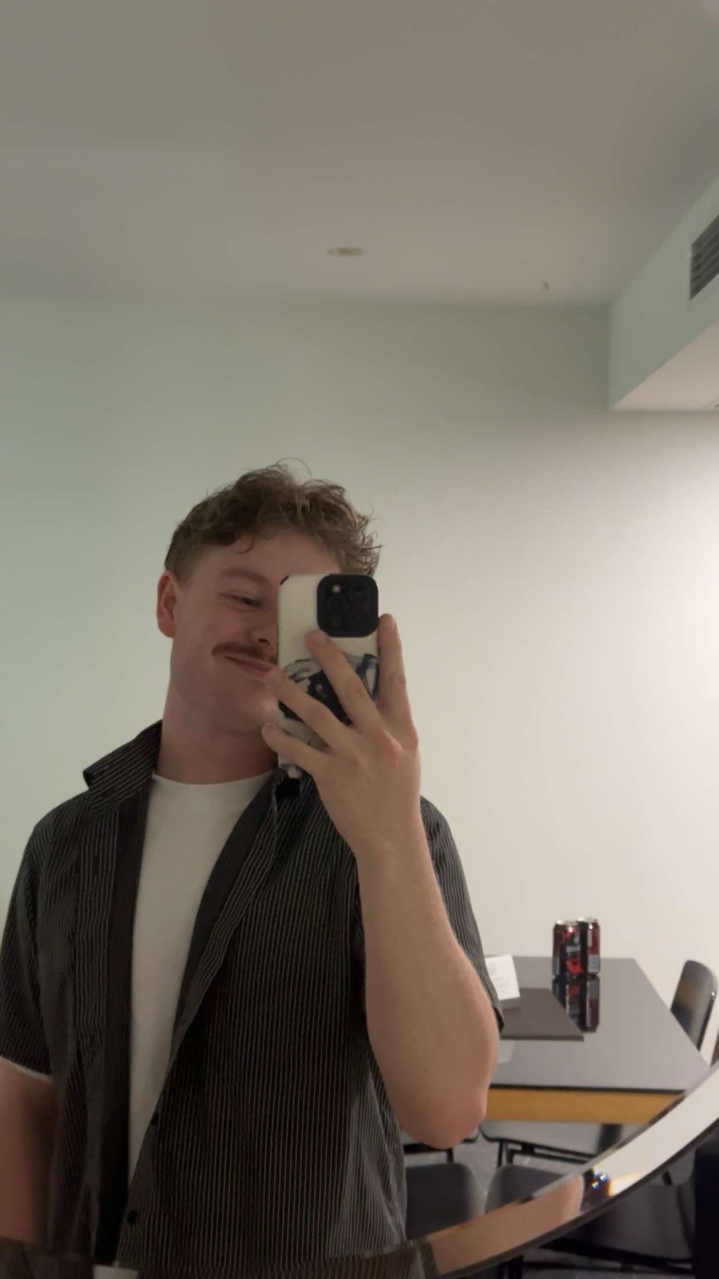 A man takes a mirror selfie. He is wearing a shirt and has a mustache.