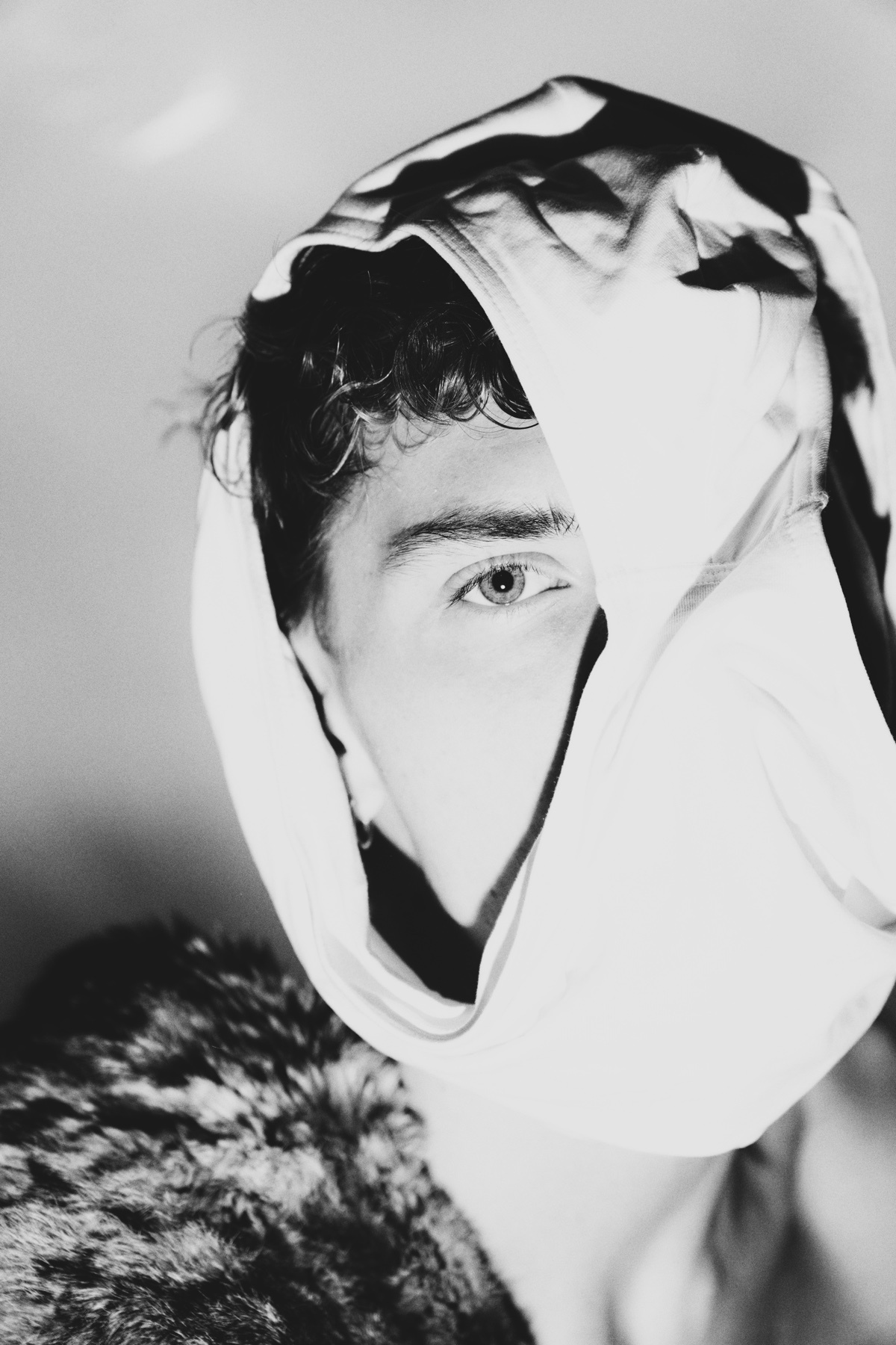 A black and white portrait of a man with curly hair. He is wearing a scarf that partially covers his face.