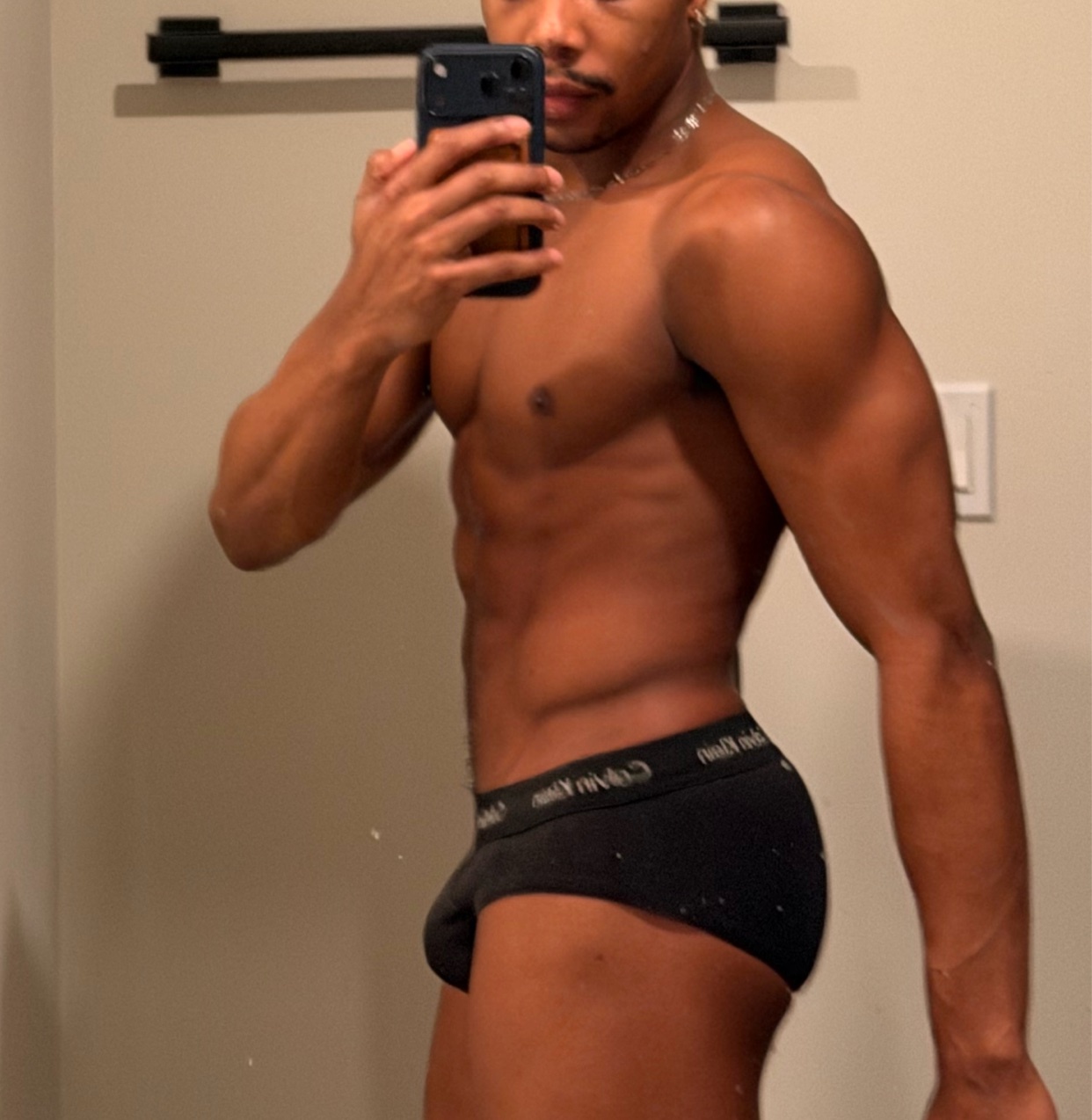 A man takes a mirror selfie, shirtless and wearing underwear. He has a muscular physique.