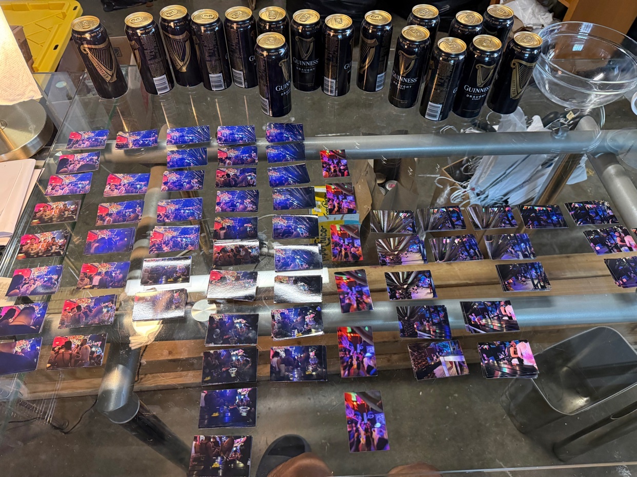 A collection of Guinness beer cans and numerous small photos of people at a party are spread across a glass table.