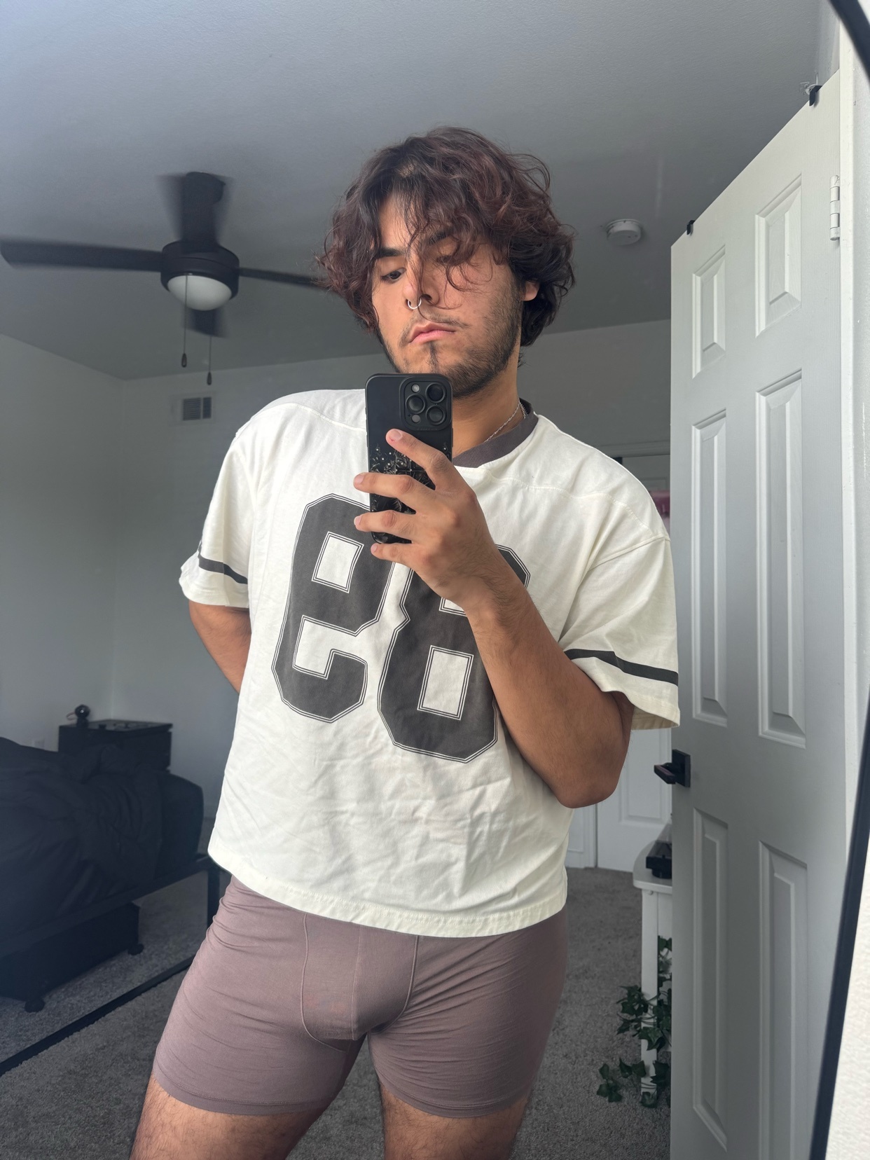 A man takes a mirror selfie in a bedroom, wearing a football jersey and underwear.