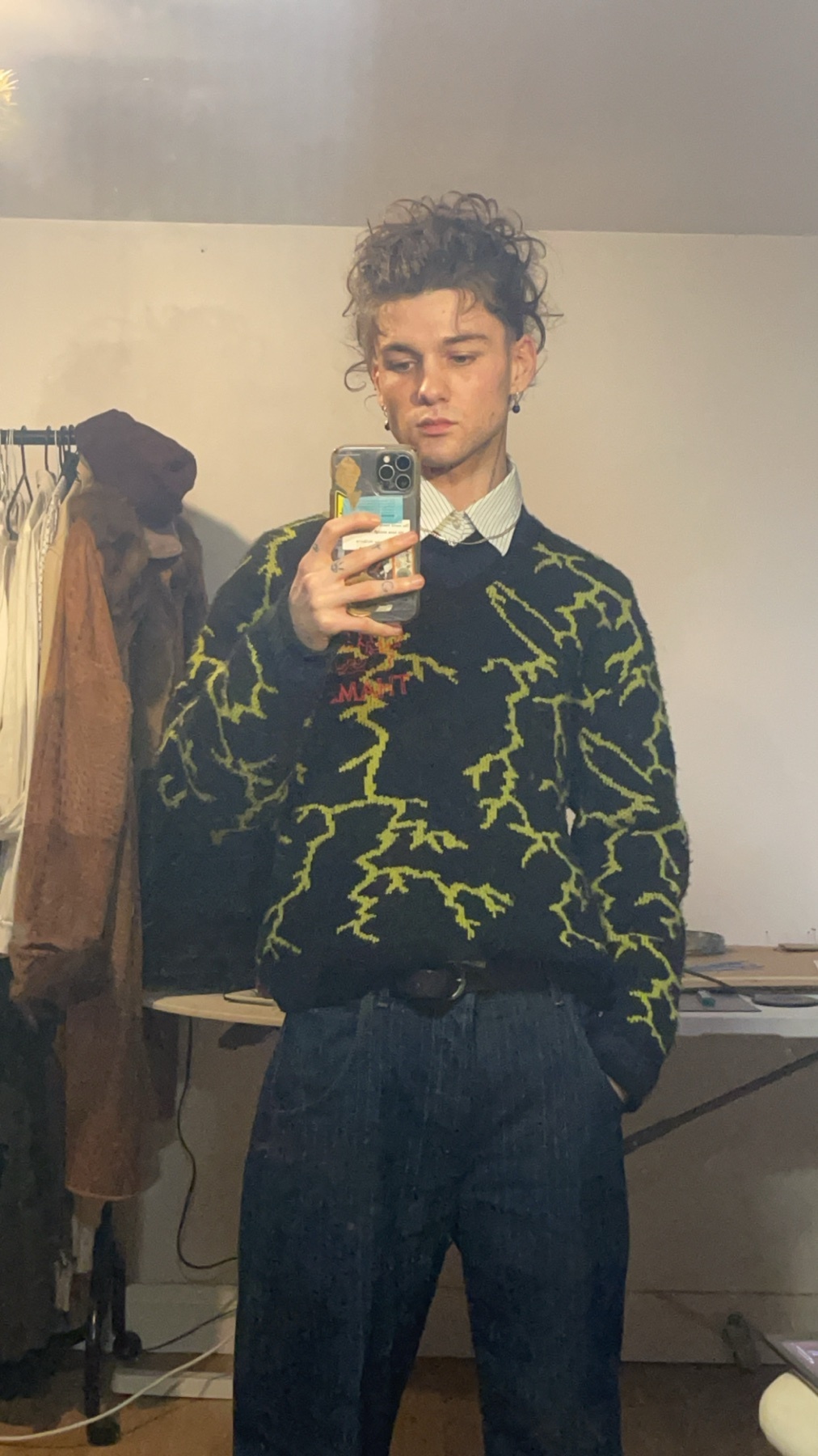 A man takes a mirror selfie. He is wearing a sweater with a lightning bolt design.