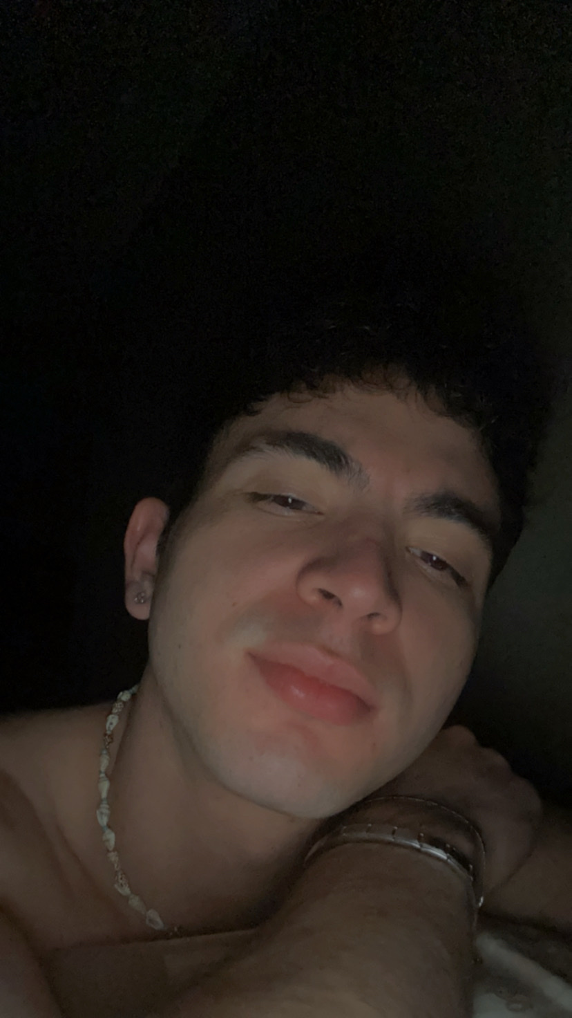 A close-up selfie of a young man with curly dark hair and a necklace.