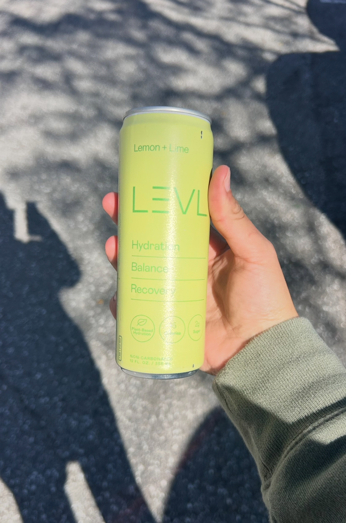 A hand holds a can of lemon-lime flavored hydration drink. The can is a bright yellow-green color.