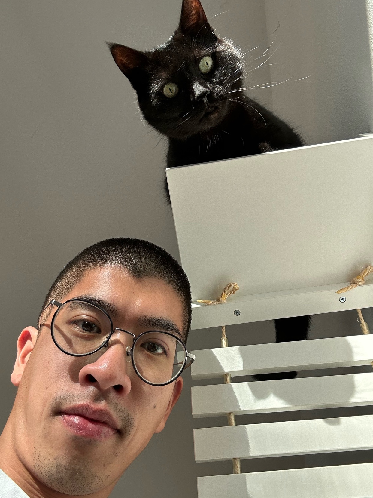 A man takes a selfie with his black cat. The cat is perched above him, looking down at the camera.