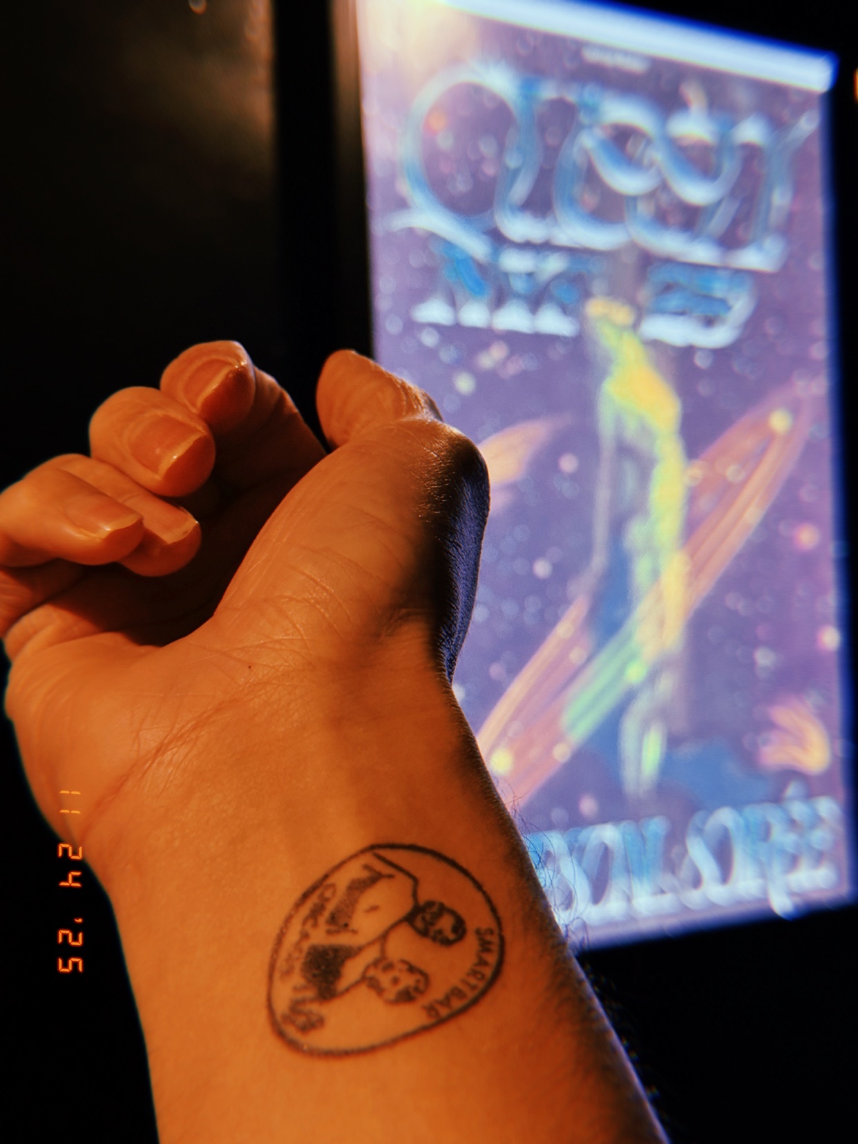 A person's arm with a Snoopy tattoo is shown in front of a colorful graphic. The image is taken in a dimly lit setting.