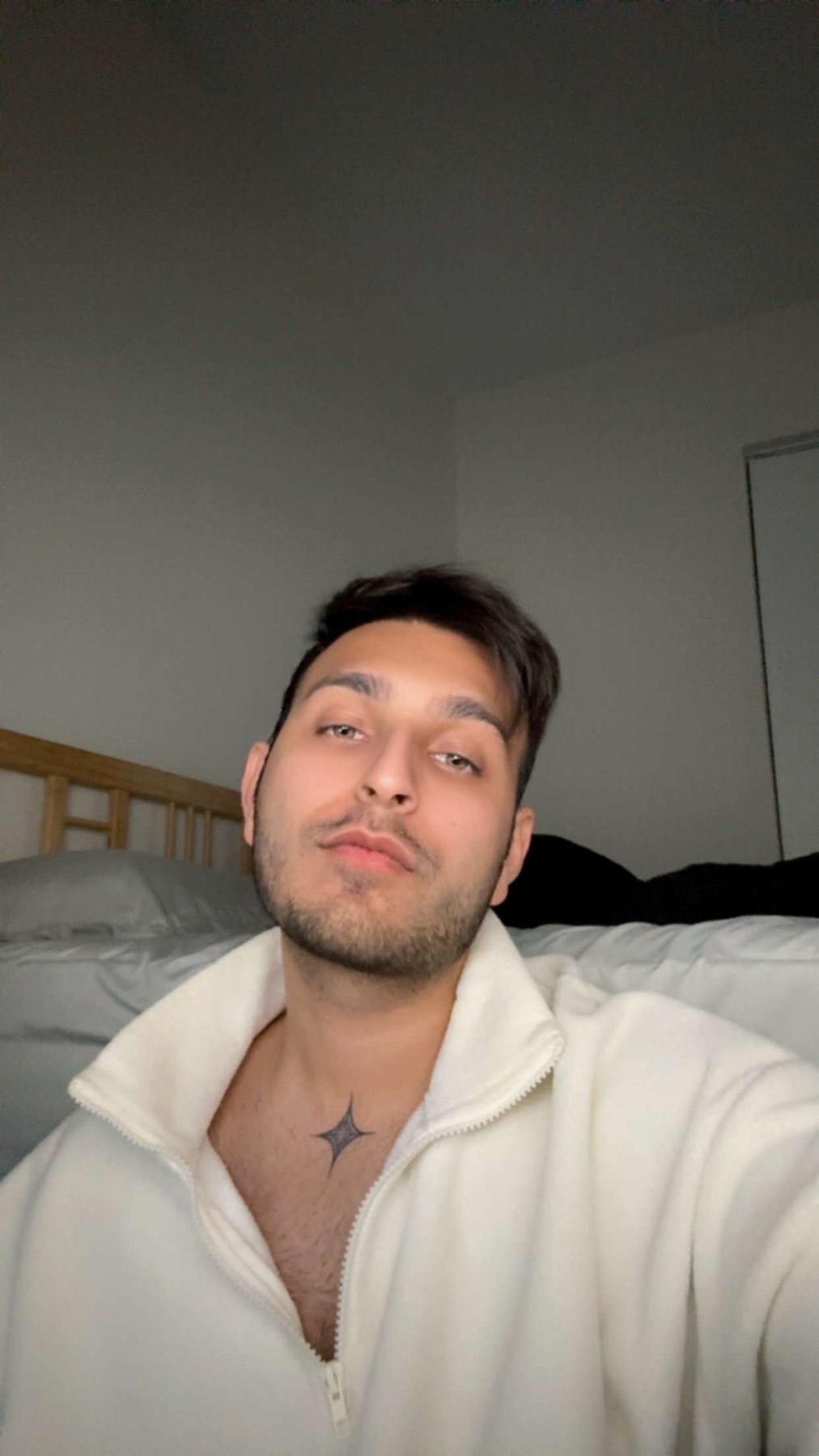 A man poses for a selfie, showcasing his style. He is shirtless and has a tattoo on his chest.