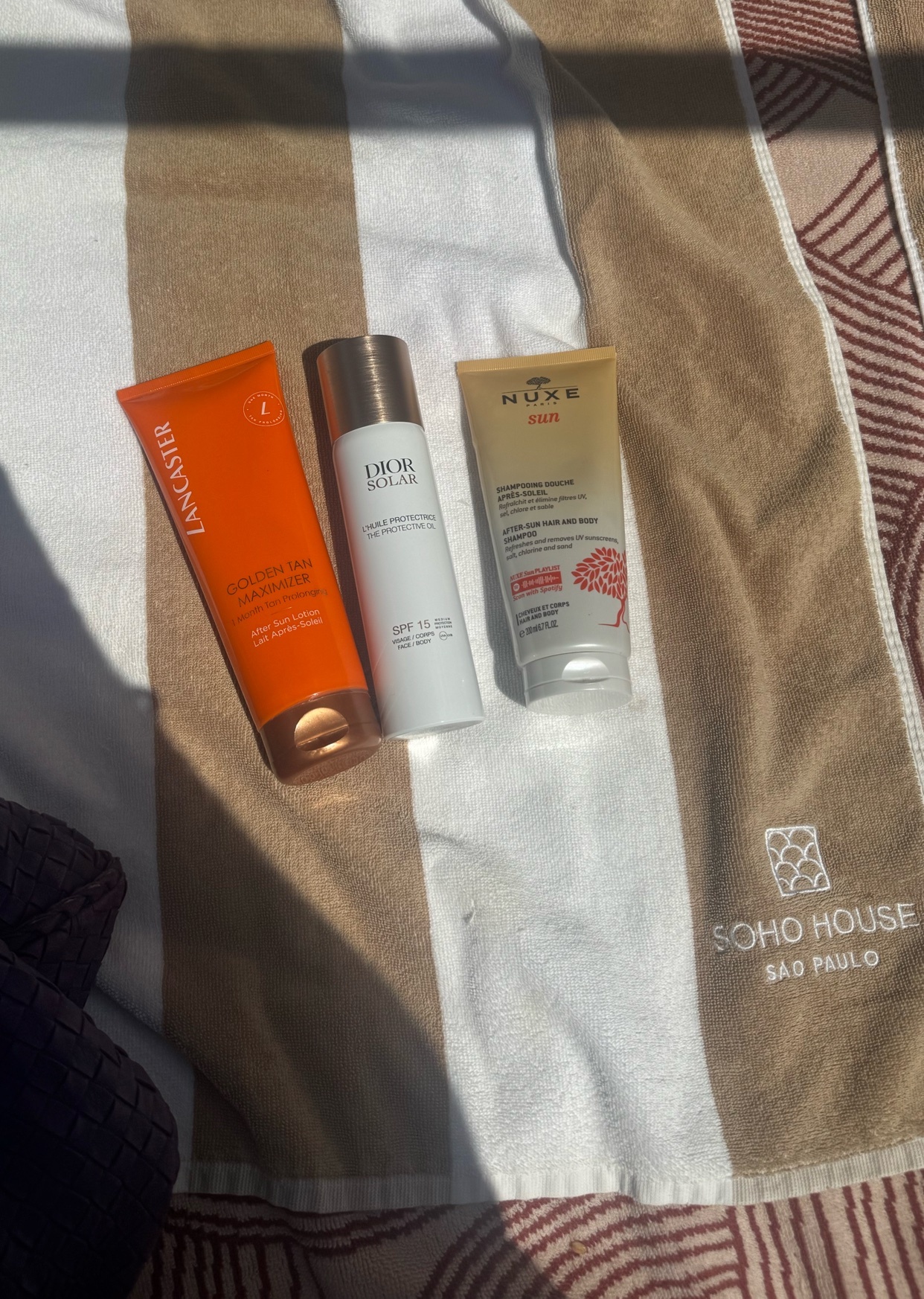 A collection of sunscreen and skincare products are displayed on a beach towel. The photo is taken in natural light, suggesting a sunny day.
