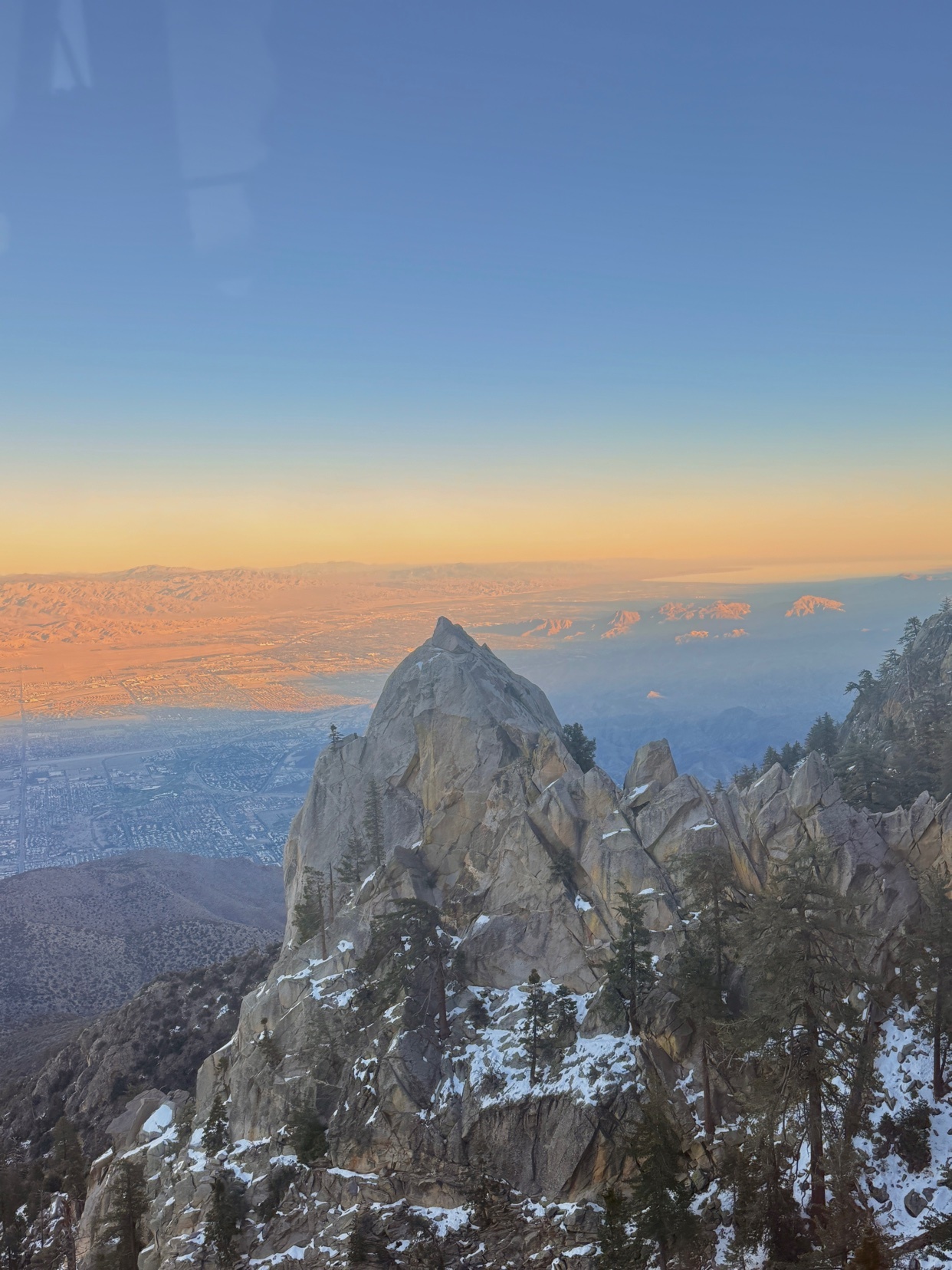A stunning view of a mountain range at sunset. The sky is a gradient of colors, and the mountains are covered in snow.